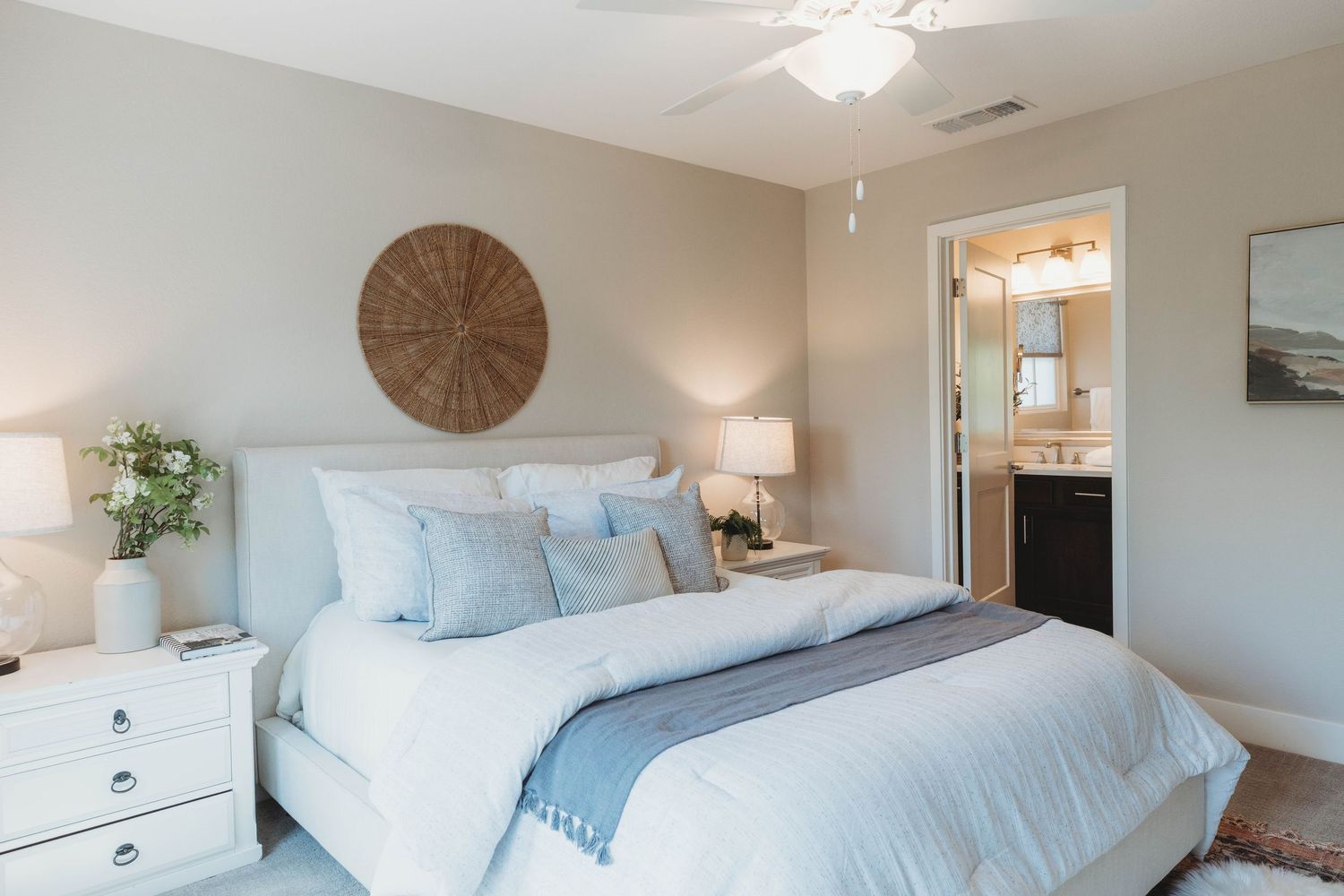 Modern bedroom with light blue bedding, white nightstands, and a circular wall clock above the headboard.