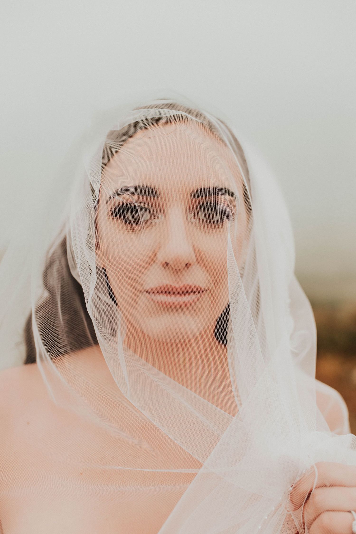 Close up portrait of a bride wearing a delicate veil against a soft, misty background.