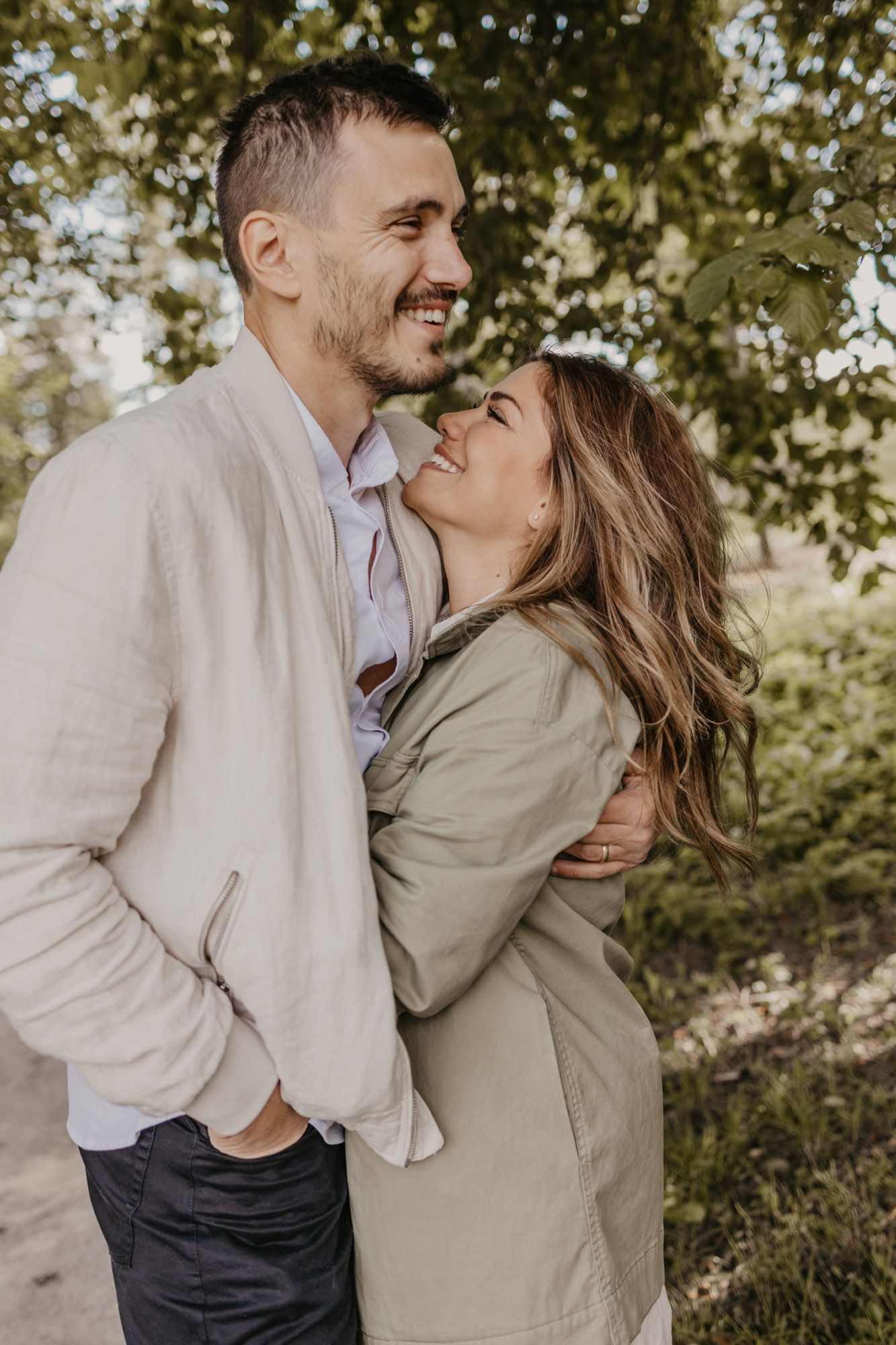 Candid laughing couple portrait against leafy green background outdoors.