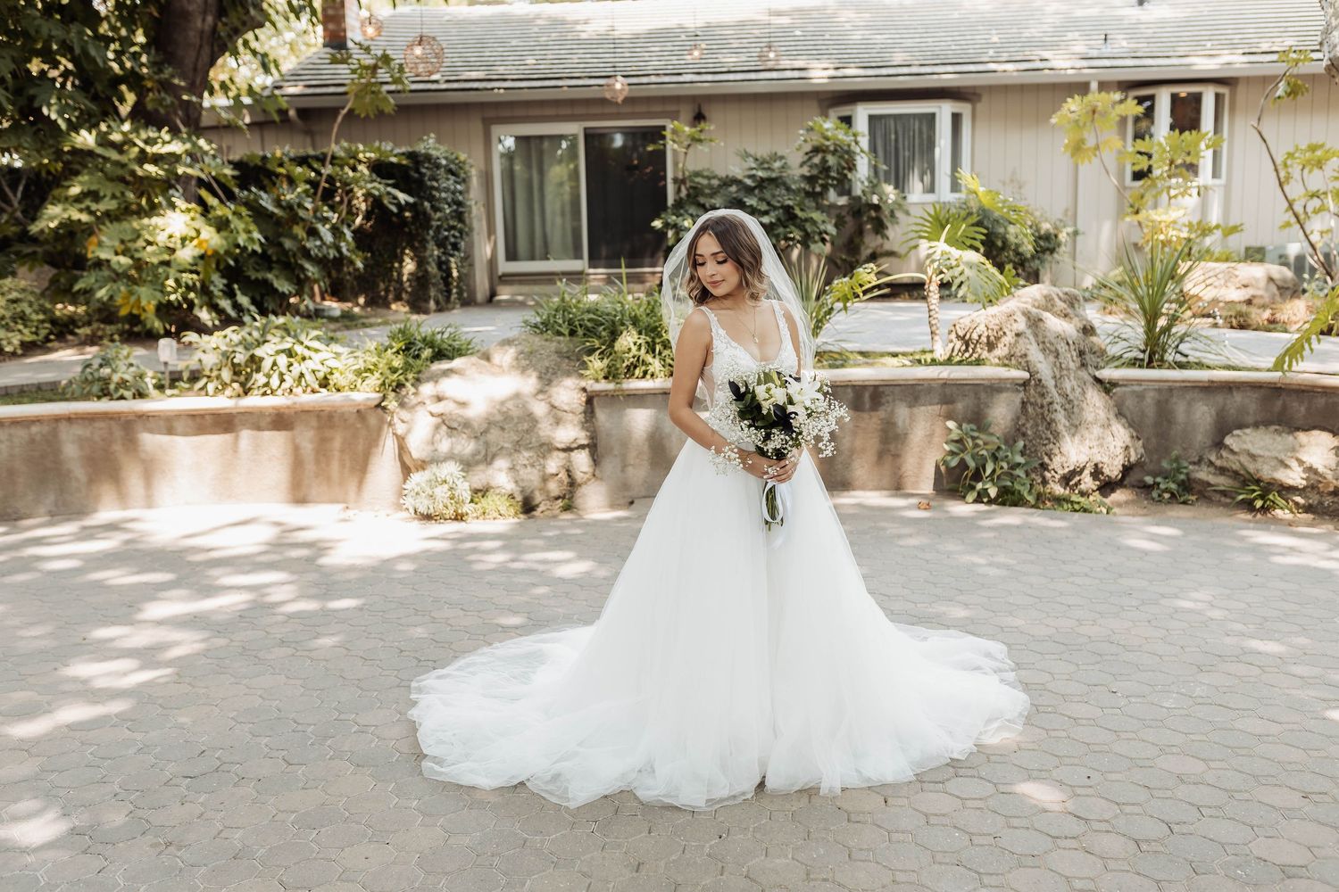 A person in a flowing white wedding dress poses gracefully in a sunlit garden setting.