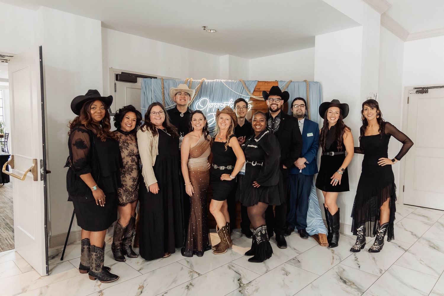 Group of stylishly dressed people posing together in black and western outfits at an indoor event.