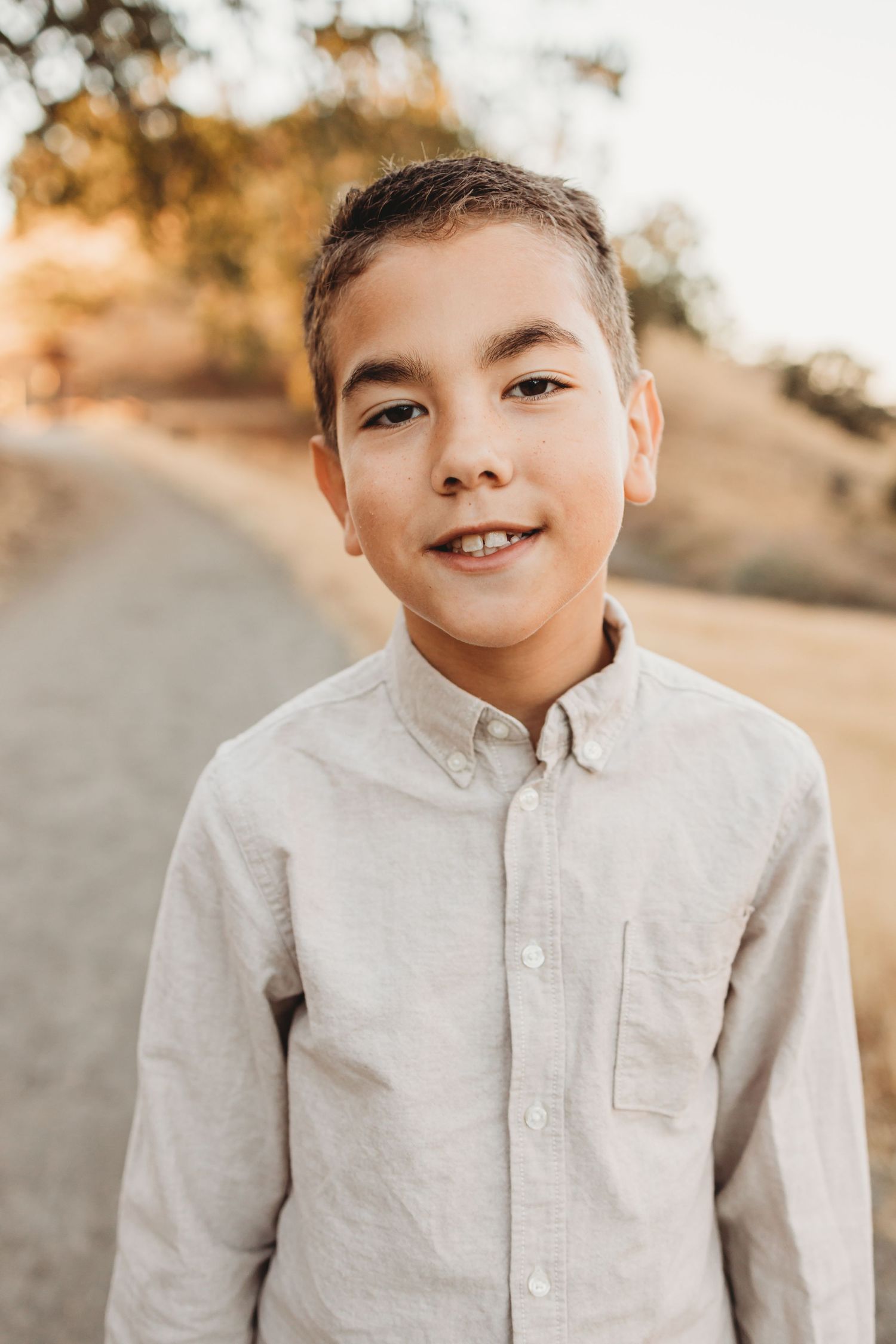 Portrait of young person in light button-down shirt smiling outdoors during golden hour.