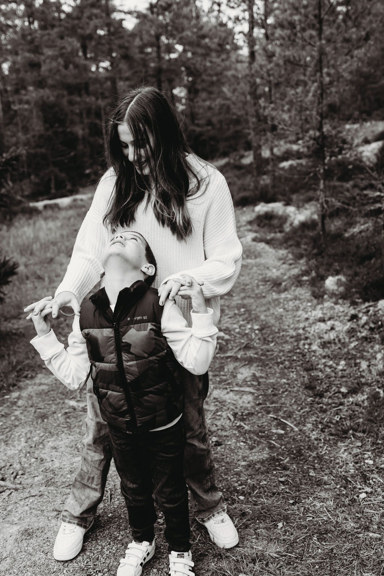 A black and white candid moment between two people on a wooded trail.