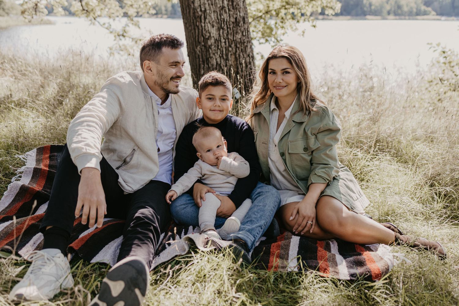 Family spending quality time together outdoors on a plaid blanket near a tree.