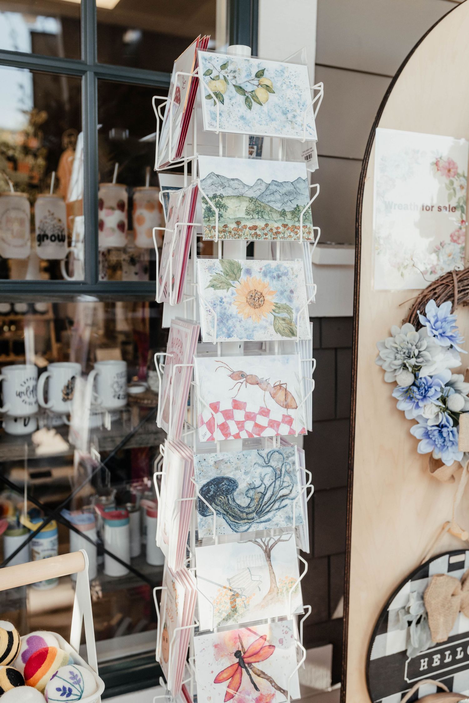 Display rack featuring decorative postcards and greeting cards with floral and scenic designs in a retail shop window.