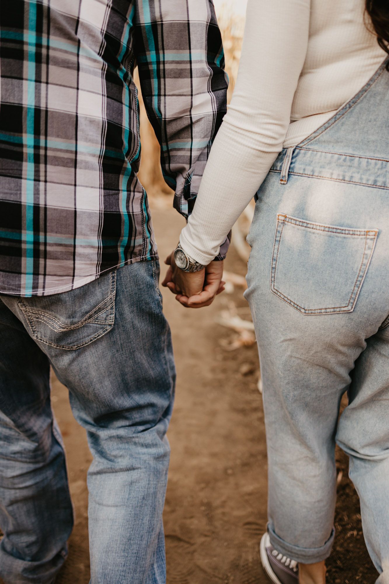 Close-up of two people holding hands while wearing casual denim and plaid clothing.