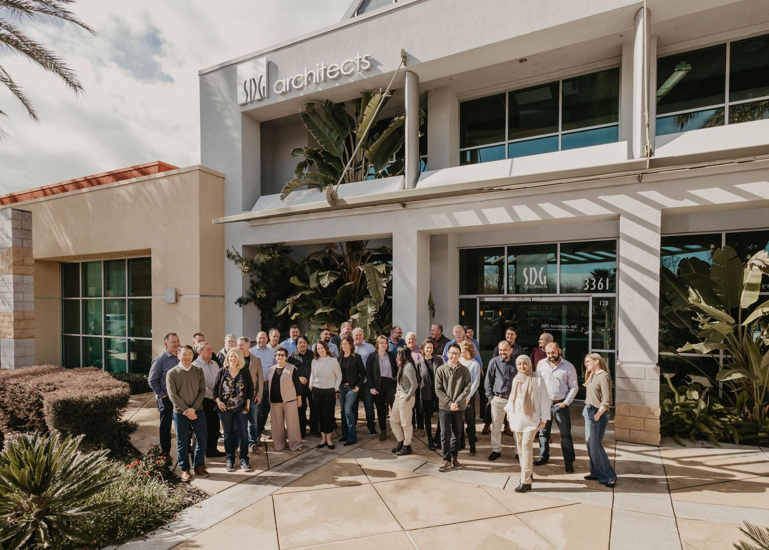 Business professionals standing together outside corporate building entrance on sunny day.