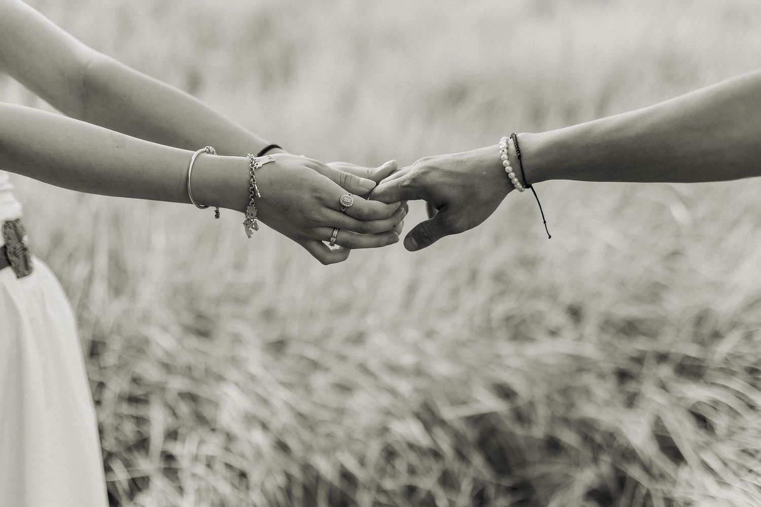 Black and white close-up of hands with bracelets reaching to touch.