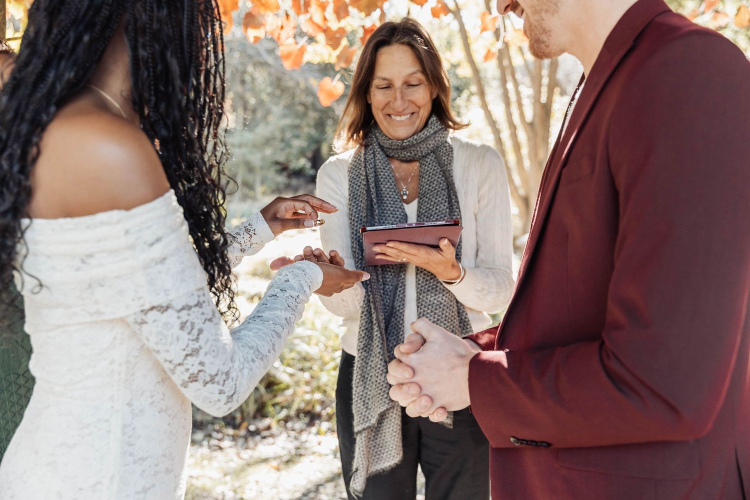 Outdoor wedding ceremony with officiant holding paperwork during ring exchange.