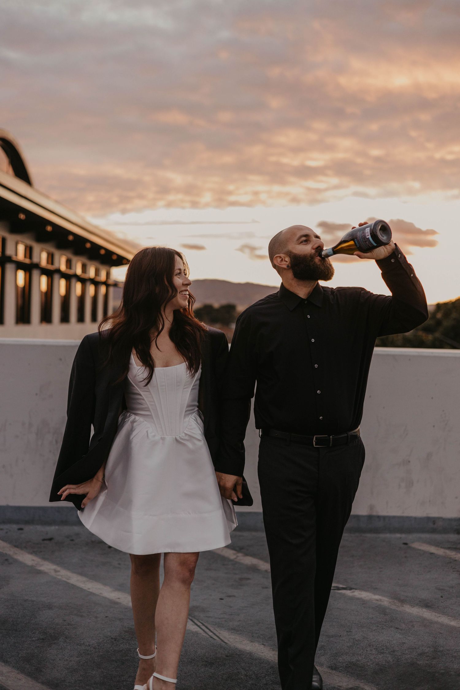A couple enjoying a sunset moment on a rooftop while one drinks from a bottle.