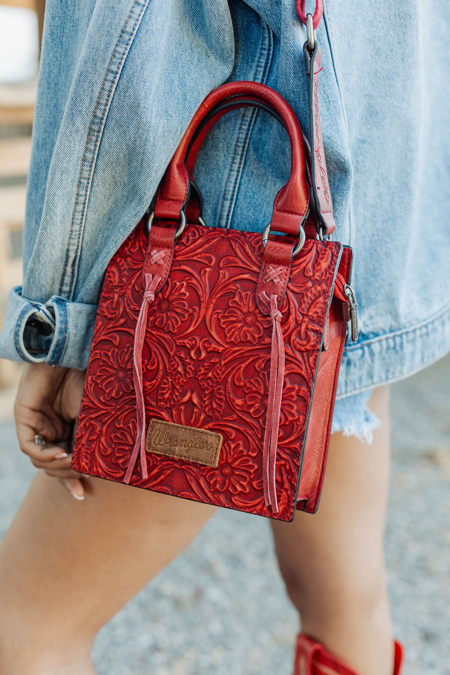 Red tooled leather handbag with decorative western floral pattern shown against light denim background.