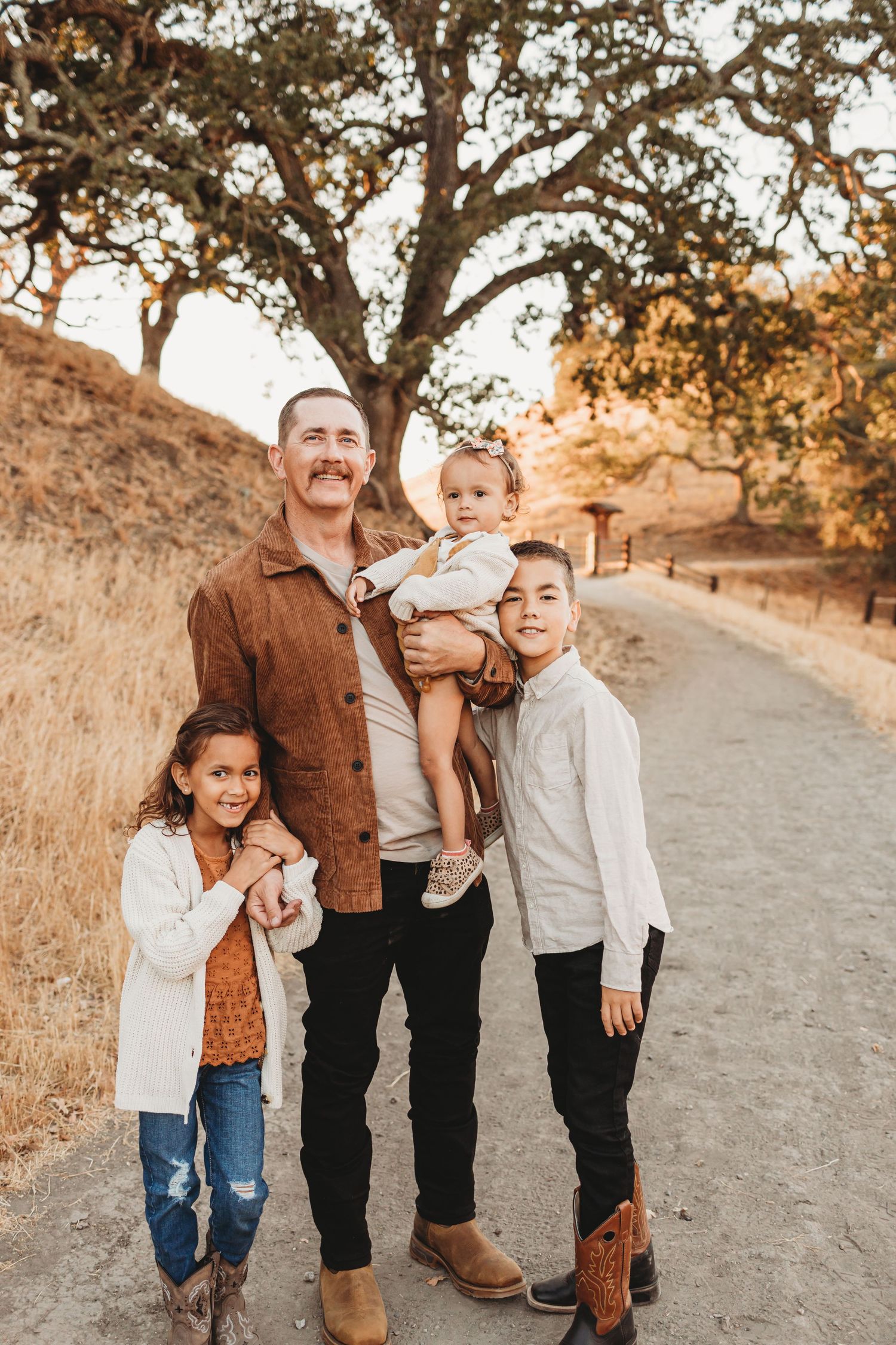 Group portrait on hiking trail with golden hills and oak tree in background during sunset.
