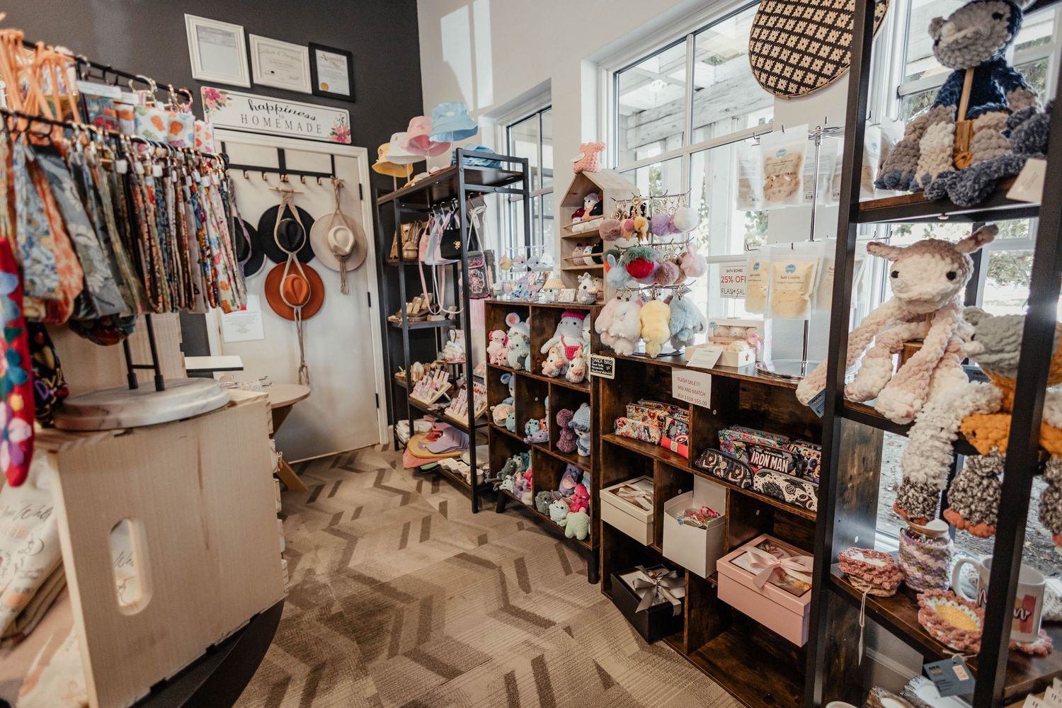 Small boutique corner featuring hanging clothes, shelved items, and decorative displays on chevron flooring.