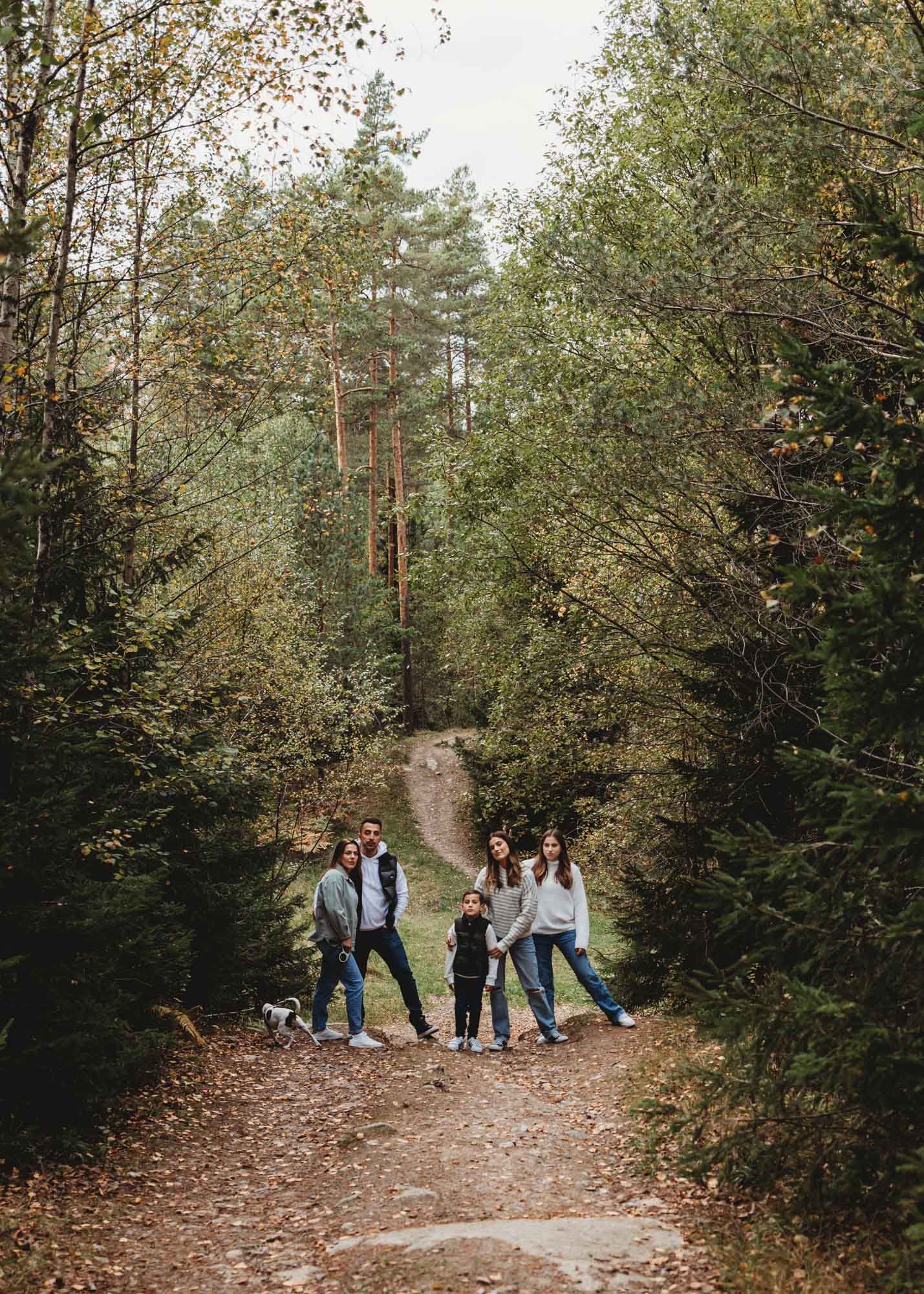 A group walking on a leaf-covered forest trail surrounded by tall trees on an autumn day.