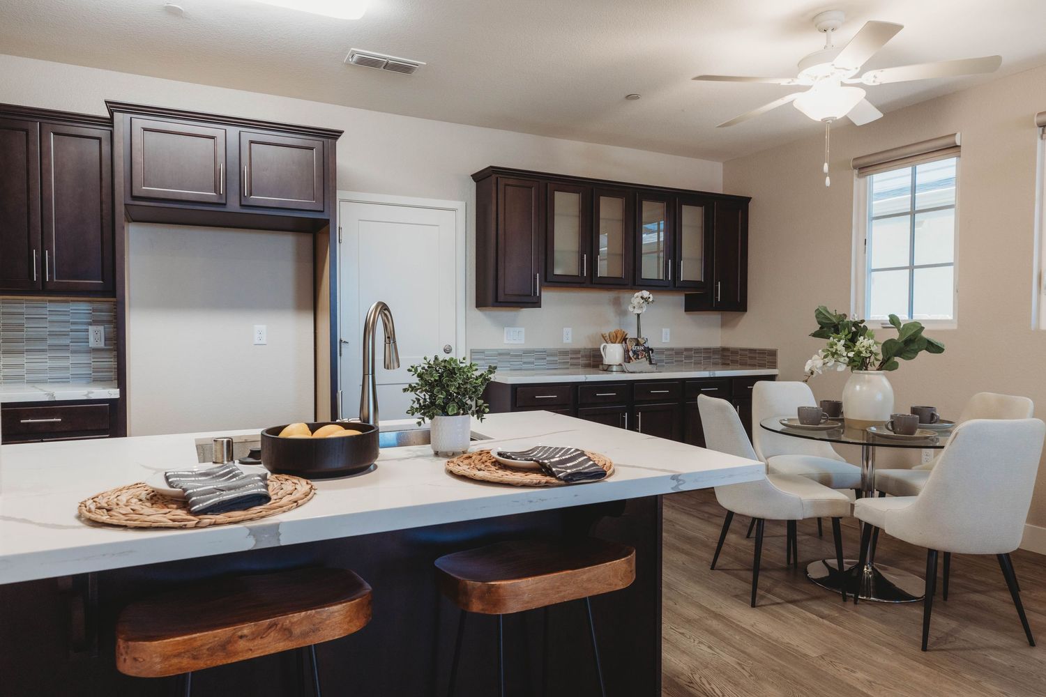 Contemporary kitchen and dining area with dark wood cabinets and white countertops.