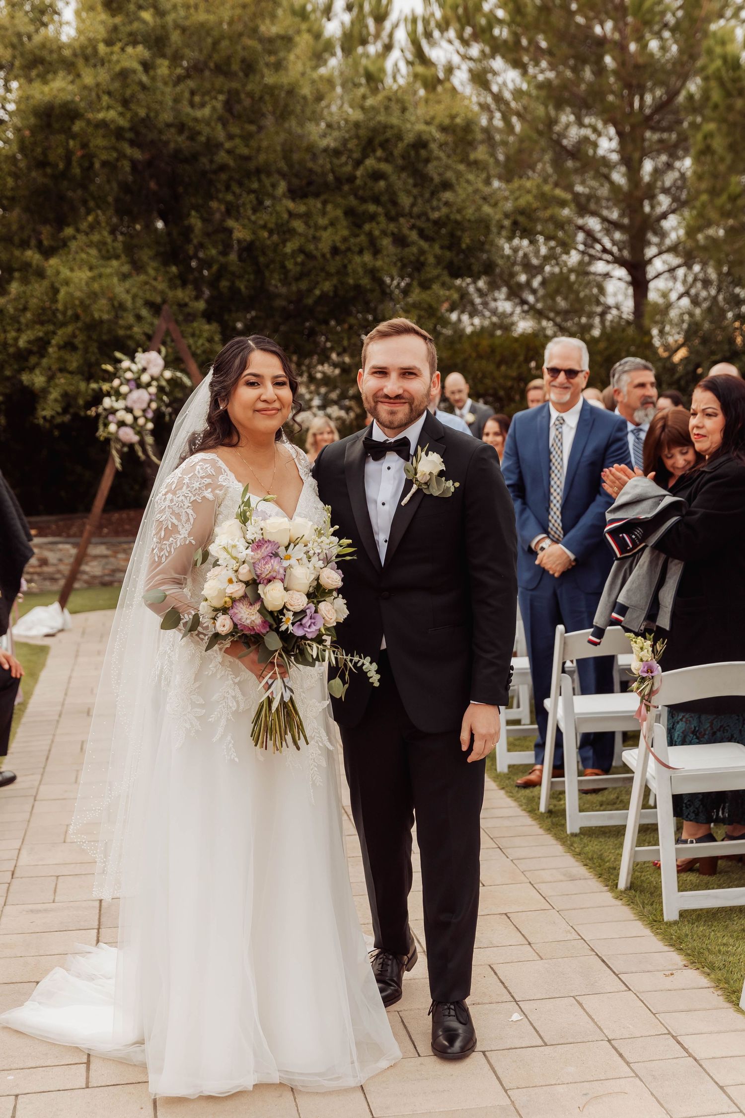 Wedding ceremony processional on stone pathway with guests seated.