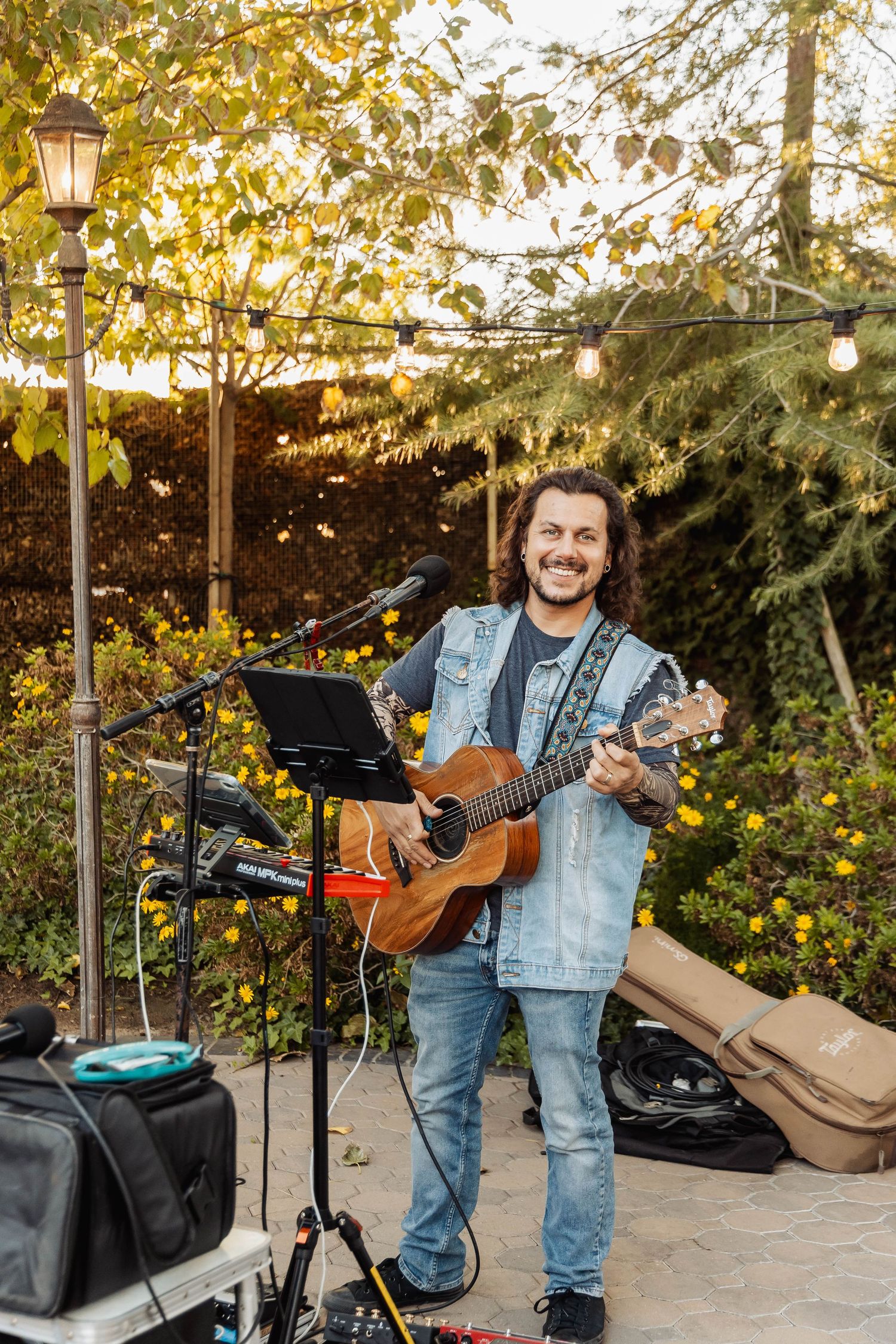 Musician performs with acoustic guitar outdoors under string lights at sunset.