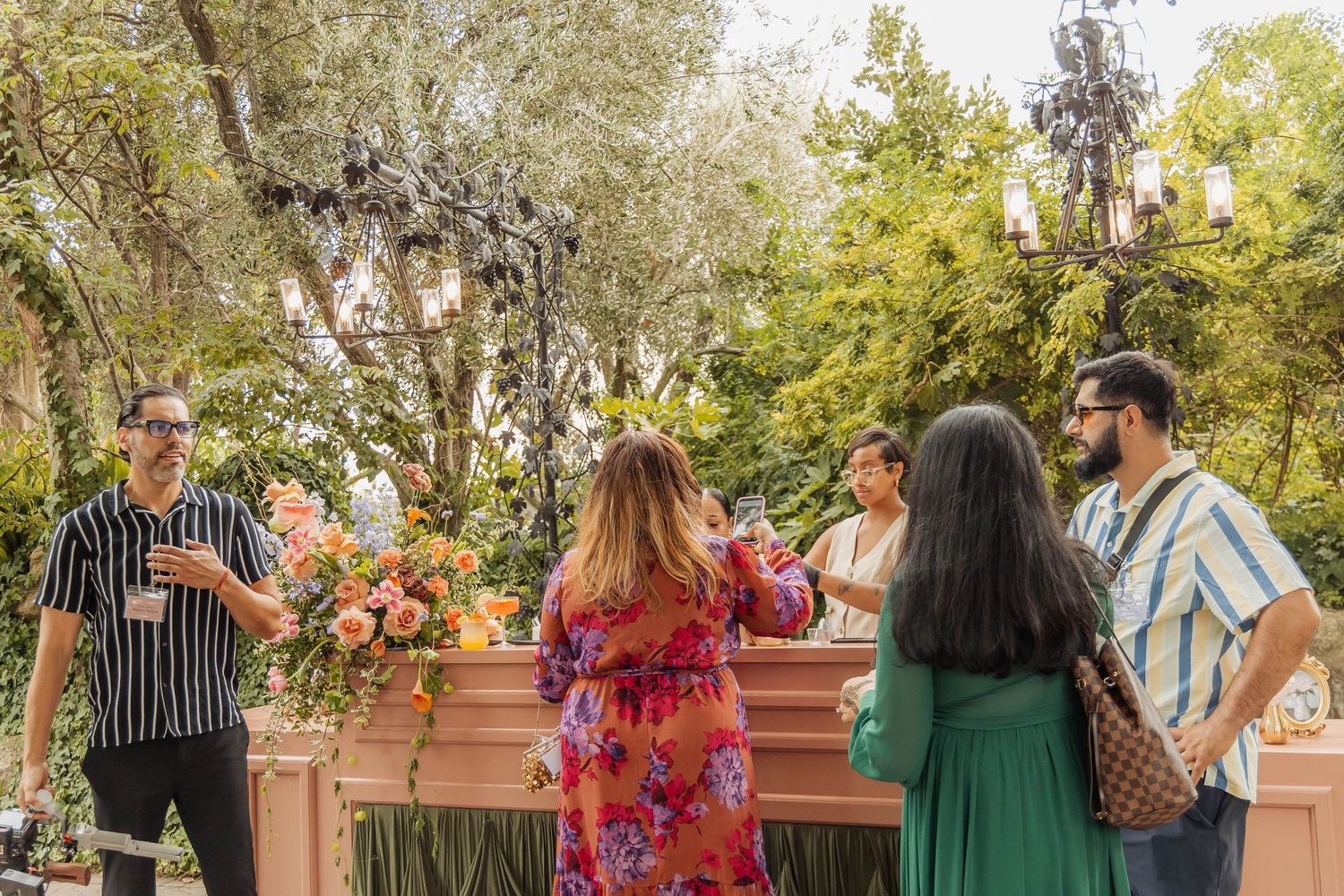 Guests mingle outdoors at an elegant garden party with floral arrangements and lush greenery.