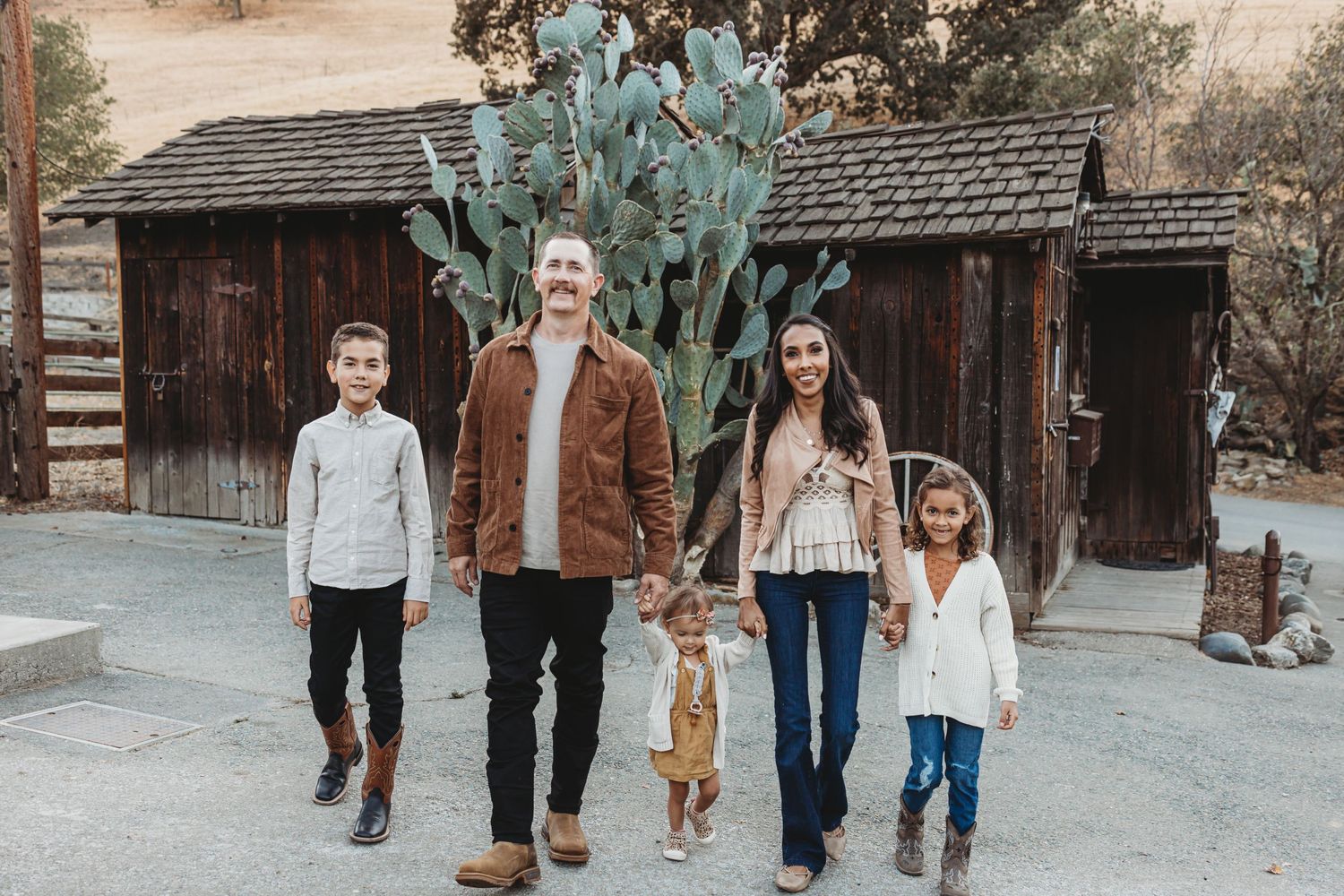 Family of five walks together near rustic wooden cabins and desert cactus.