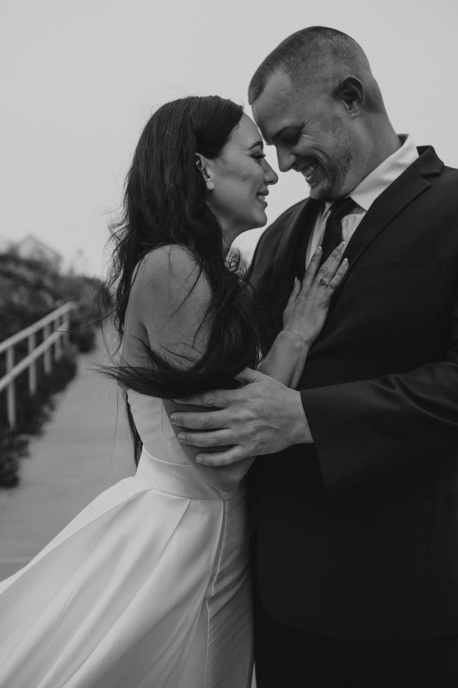 Black and white portrait of a couple sharing a joyful moment in wedding attire.