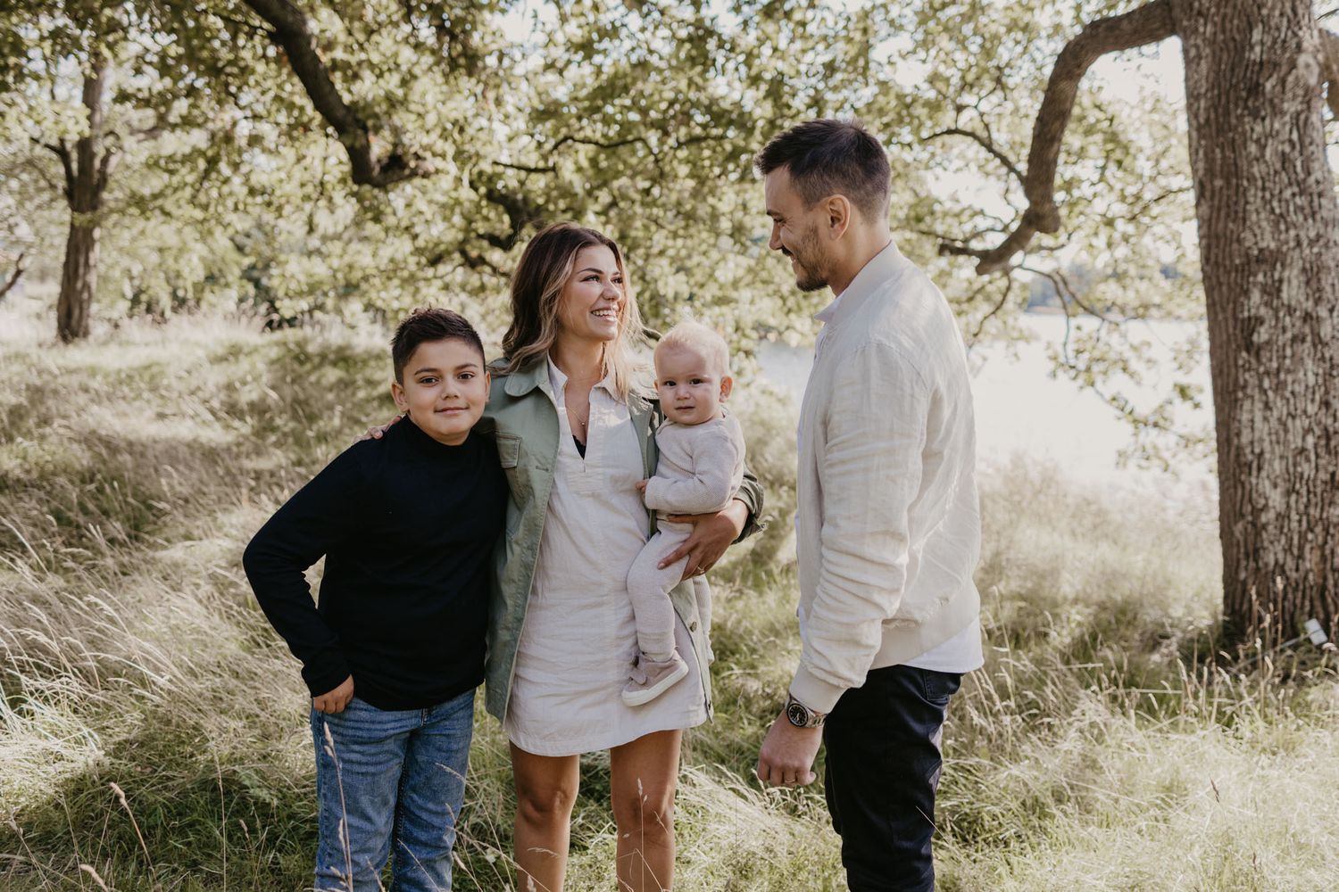 Family of four enjoying a sunny day outdoors under trees with natural sunlight filtering through.