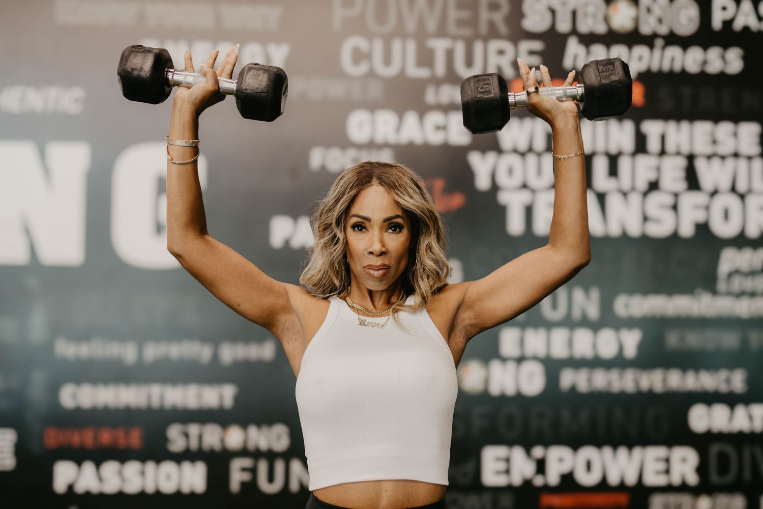 Woman exercising with dumbbells in front of wall with inspirational fitness quotes.