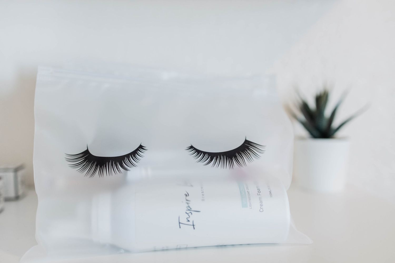 False eyelashes displayed on white paper with small succulent plant in background.