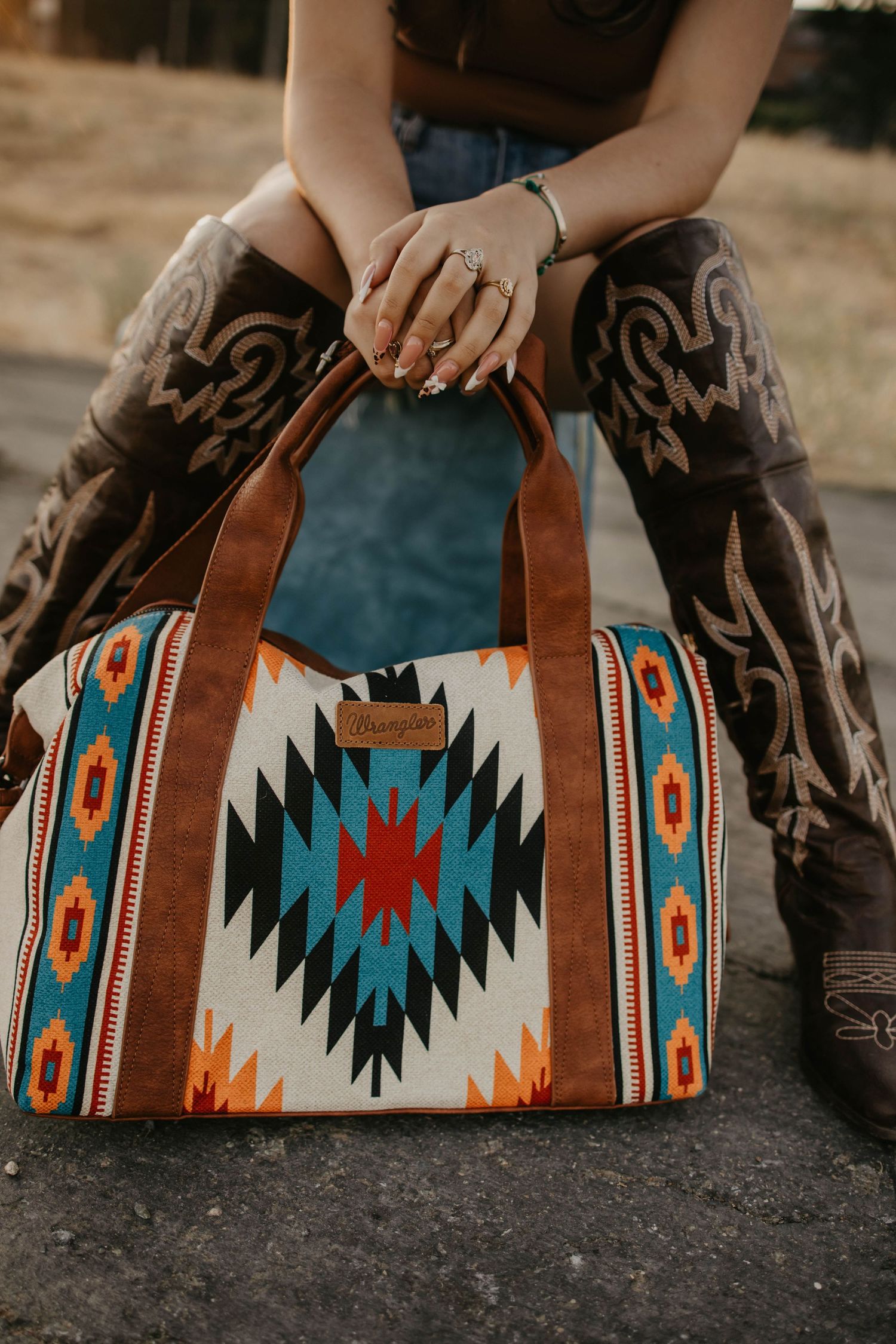 Southwestern print duffel bag with turquoise and orange aztec pattern shown with cowboy boots.
