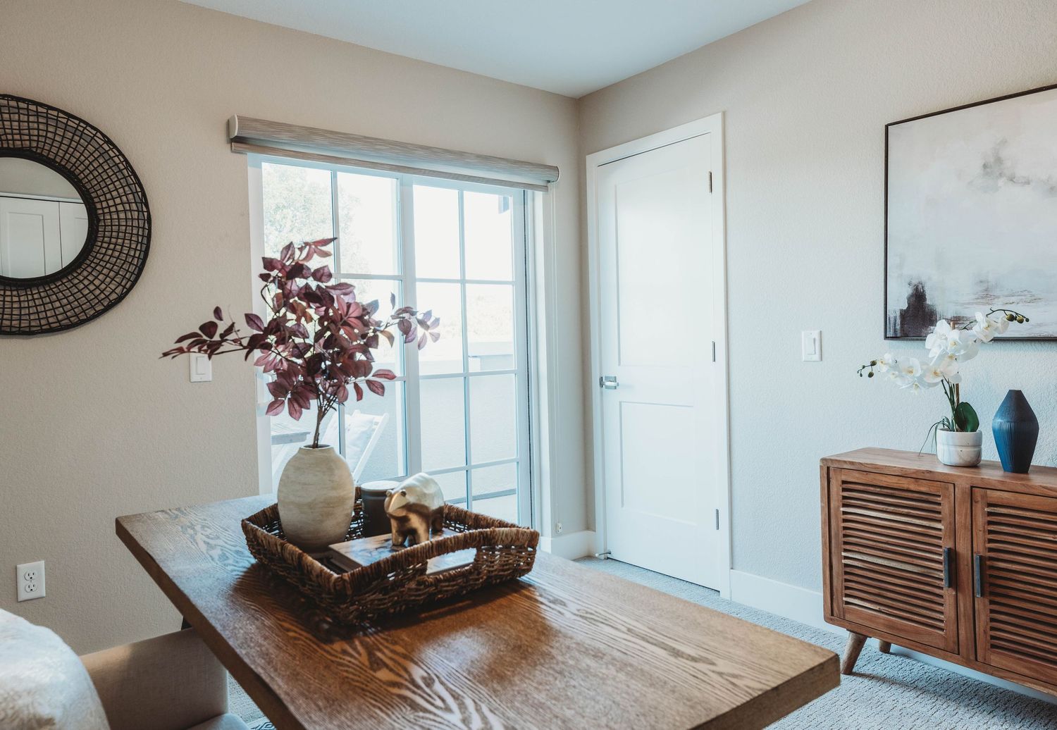 Modern dining area with wooden table, round mirror, and decorative branches in vase.