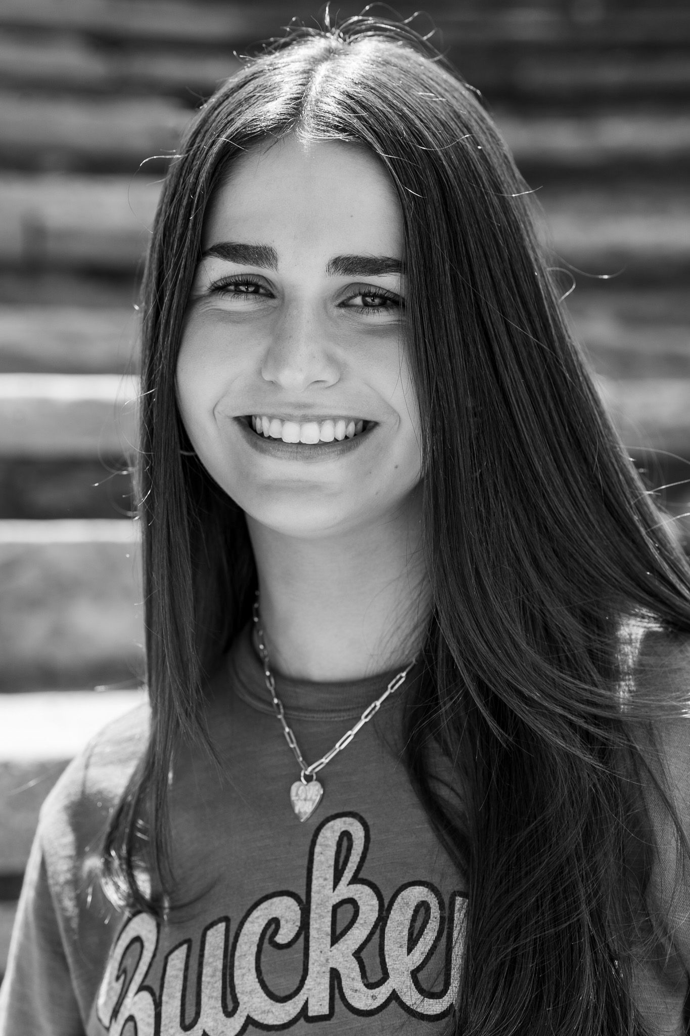 Black and white portrait of a smiling young woman with long dark hair wearing a Buckeyes t-shirt and heart necklace.