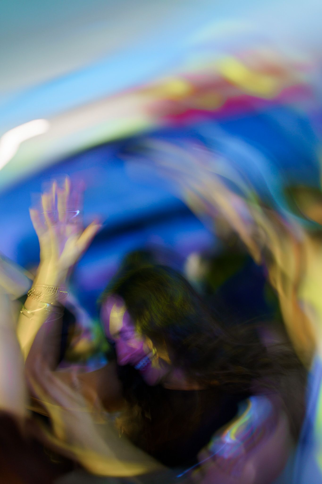 Blurred motion photo of people dancing at a vibrant party with colorful lights and raised hands.