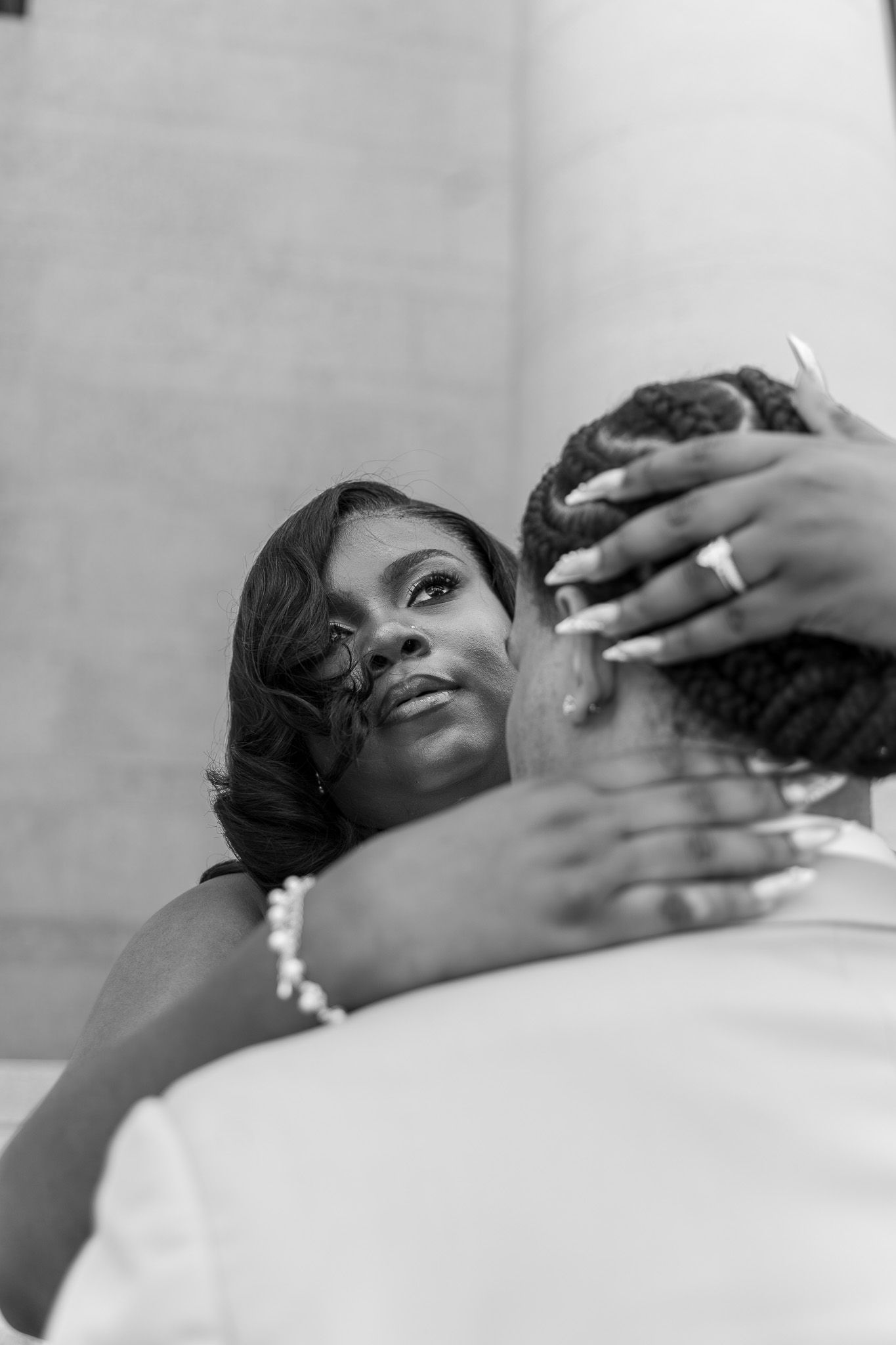 Black and white photo of a woman gazing lovingly at a man while embracing him, wearing a pearl bracelet and ring.