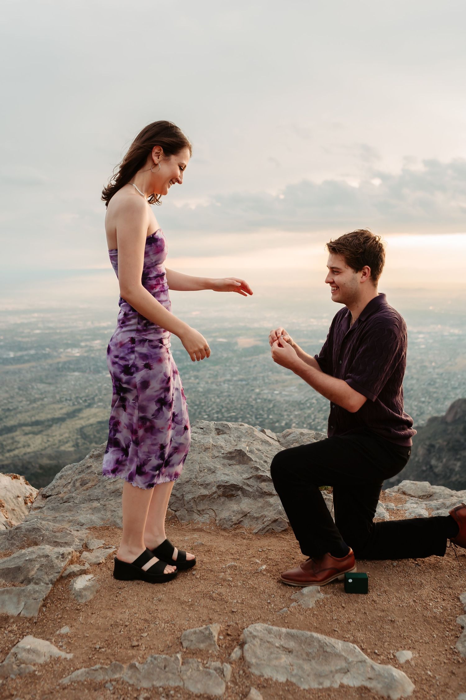 A romantic proposal moment captured on a mountain cliff during sunset.