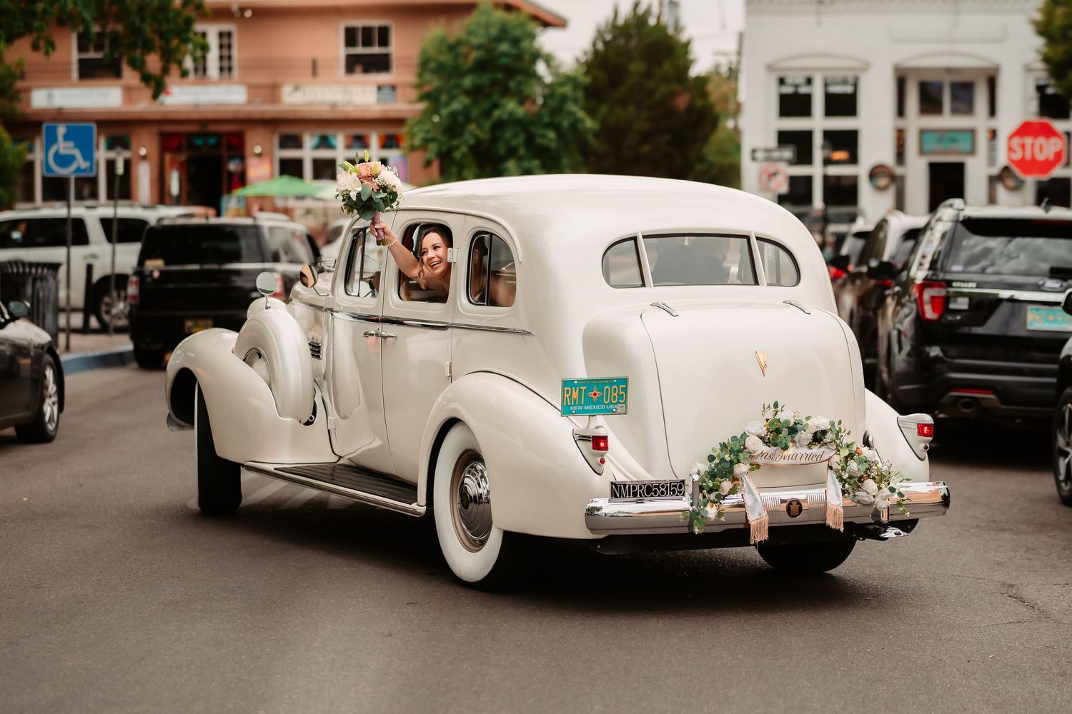 A row of vintage cream-colored wedding cars parked on a city street.