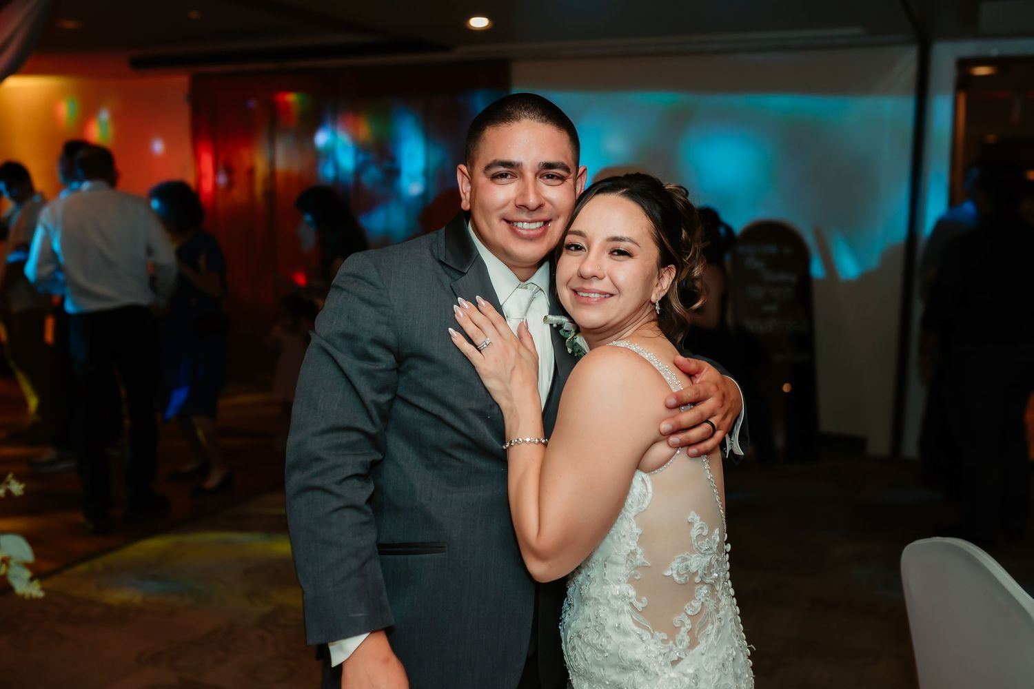 Happy couple embraces on their wedding day with colorful lighting in the background.