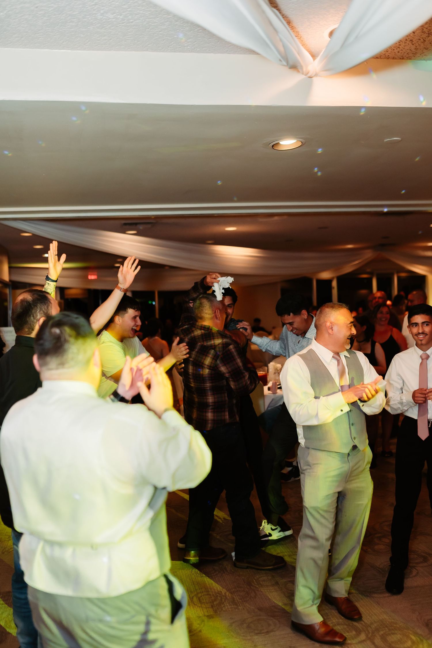 Wedding guests dance and celebrate under draped fabric ceiling decorations at an indoor reception.