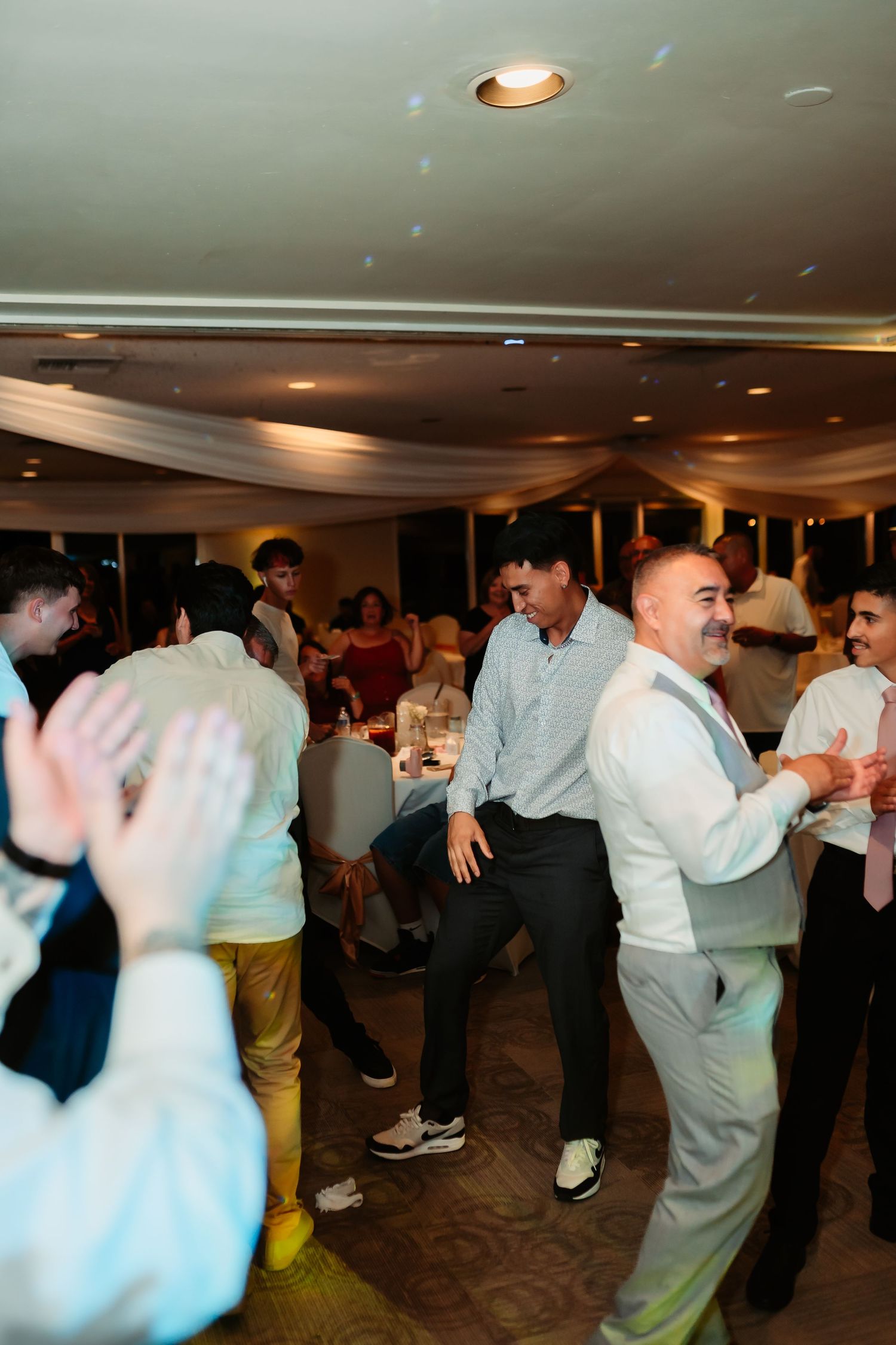 Wedding guests dancing in a lively reception with warm lighting and casual attire.
