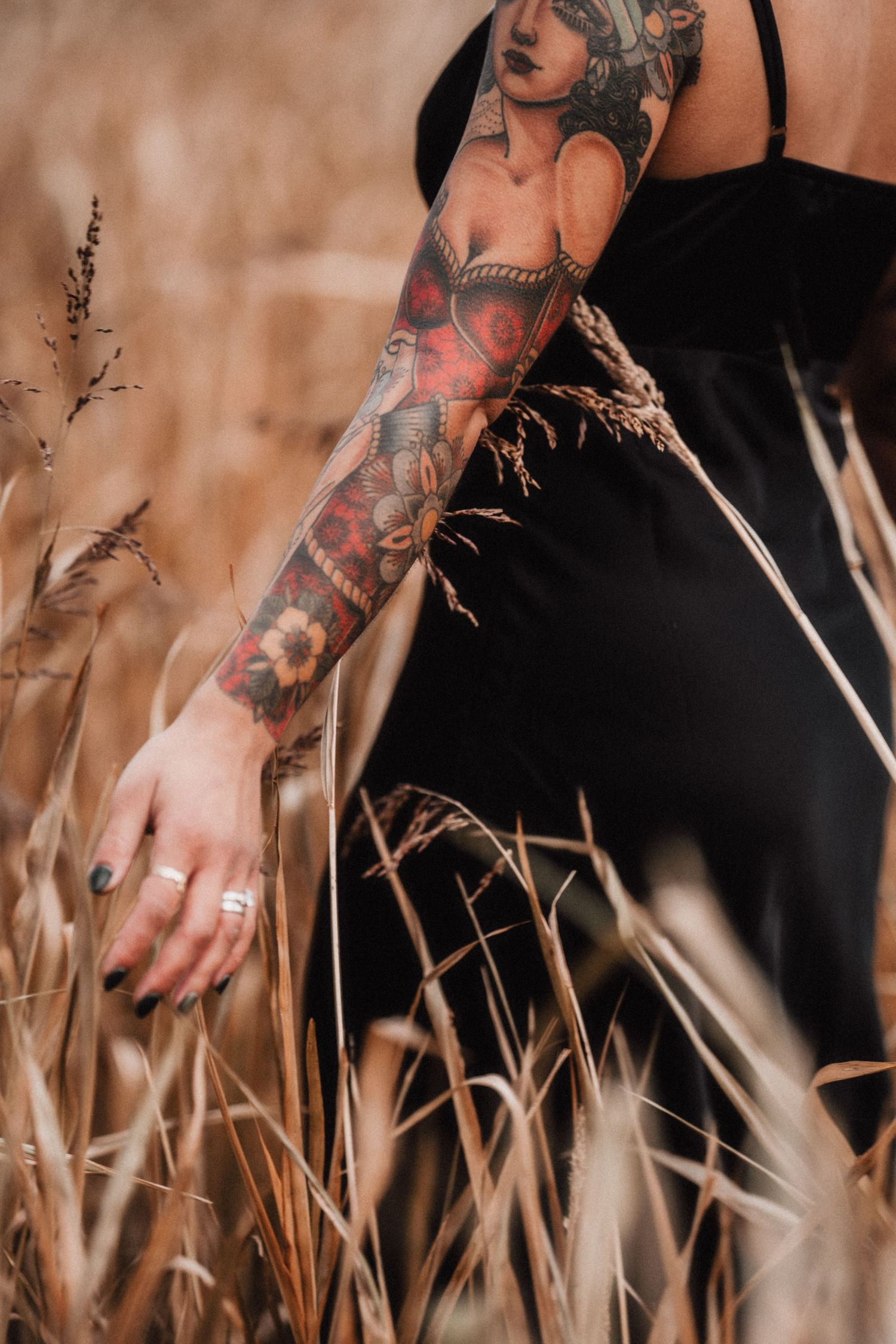 Tattooed arms reach through tall dried grass stalks in an artistic outdoor photography composition.