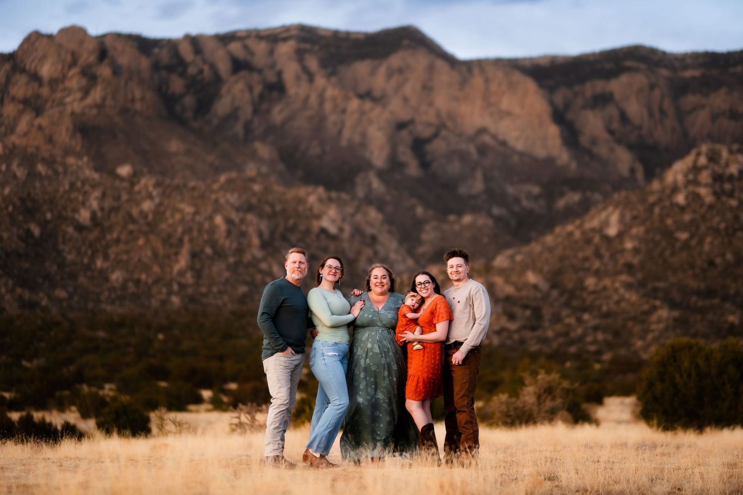 A group of people stands together against a scenic mountain backdrop in warm afternoon light.