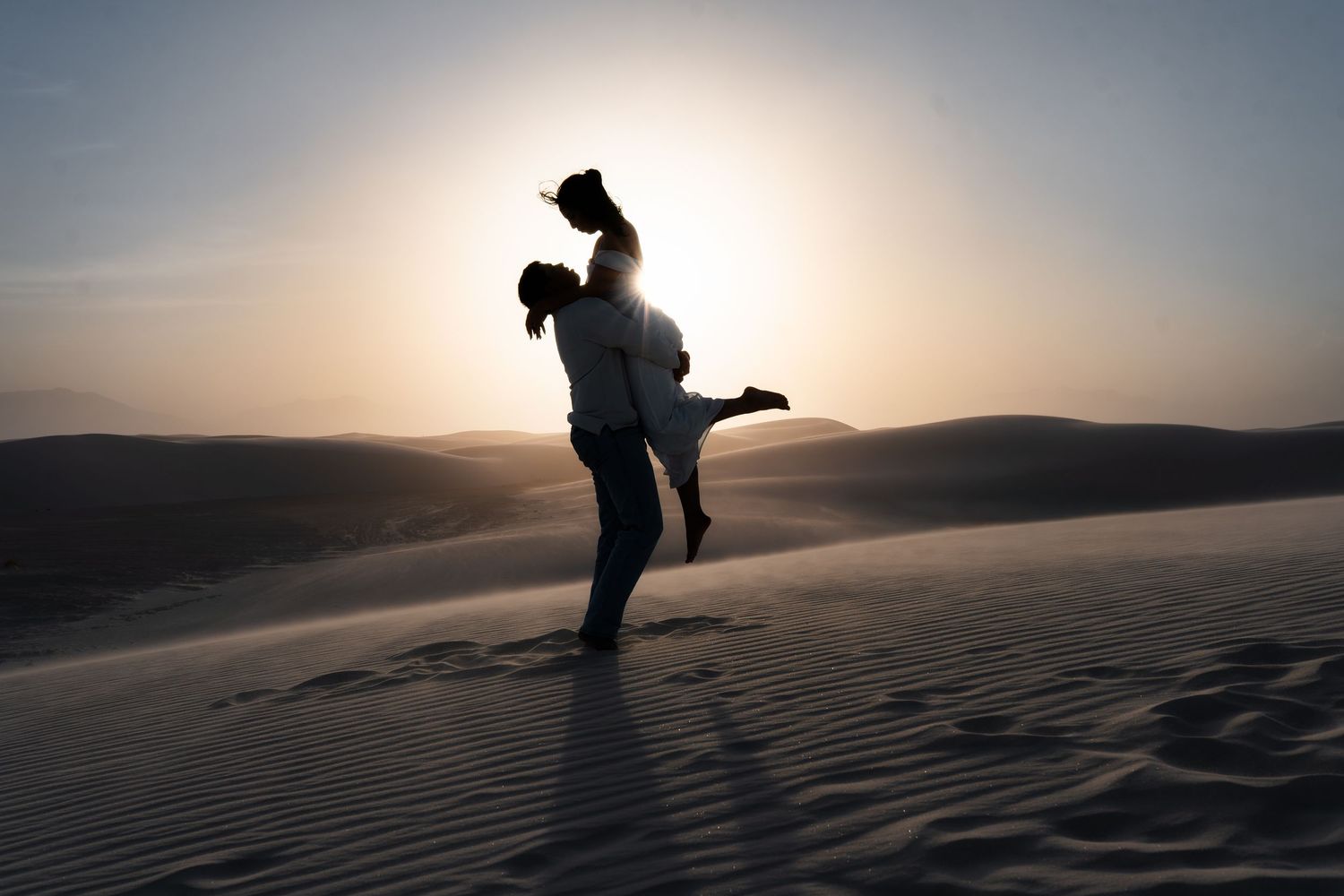 Silhouetted figures dance and play on sand dunes during a misty golden sunset.