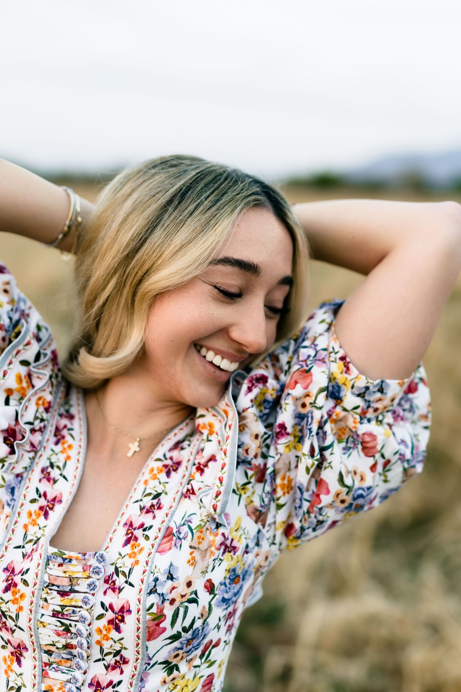 Happy young woman in floral dress laughing outdoors in golden field.