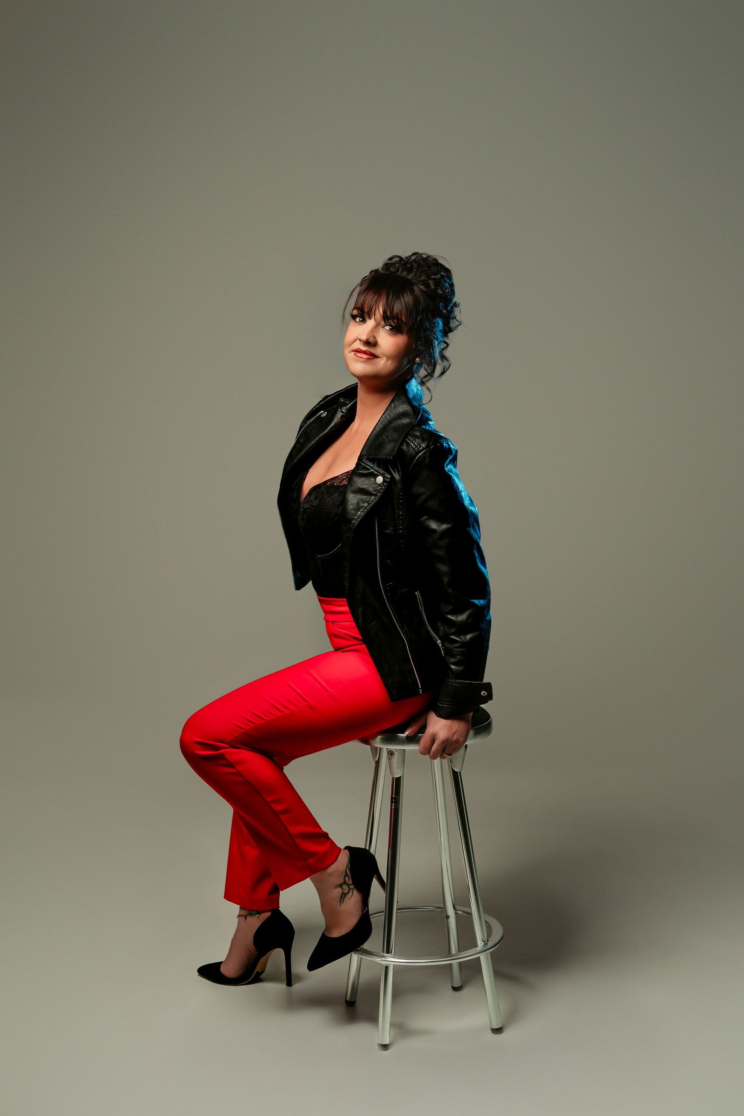 Fashion portrait series featuring black leather jacket and red pants against neutral backdrop with metal stool.