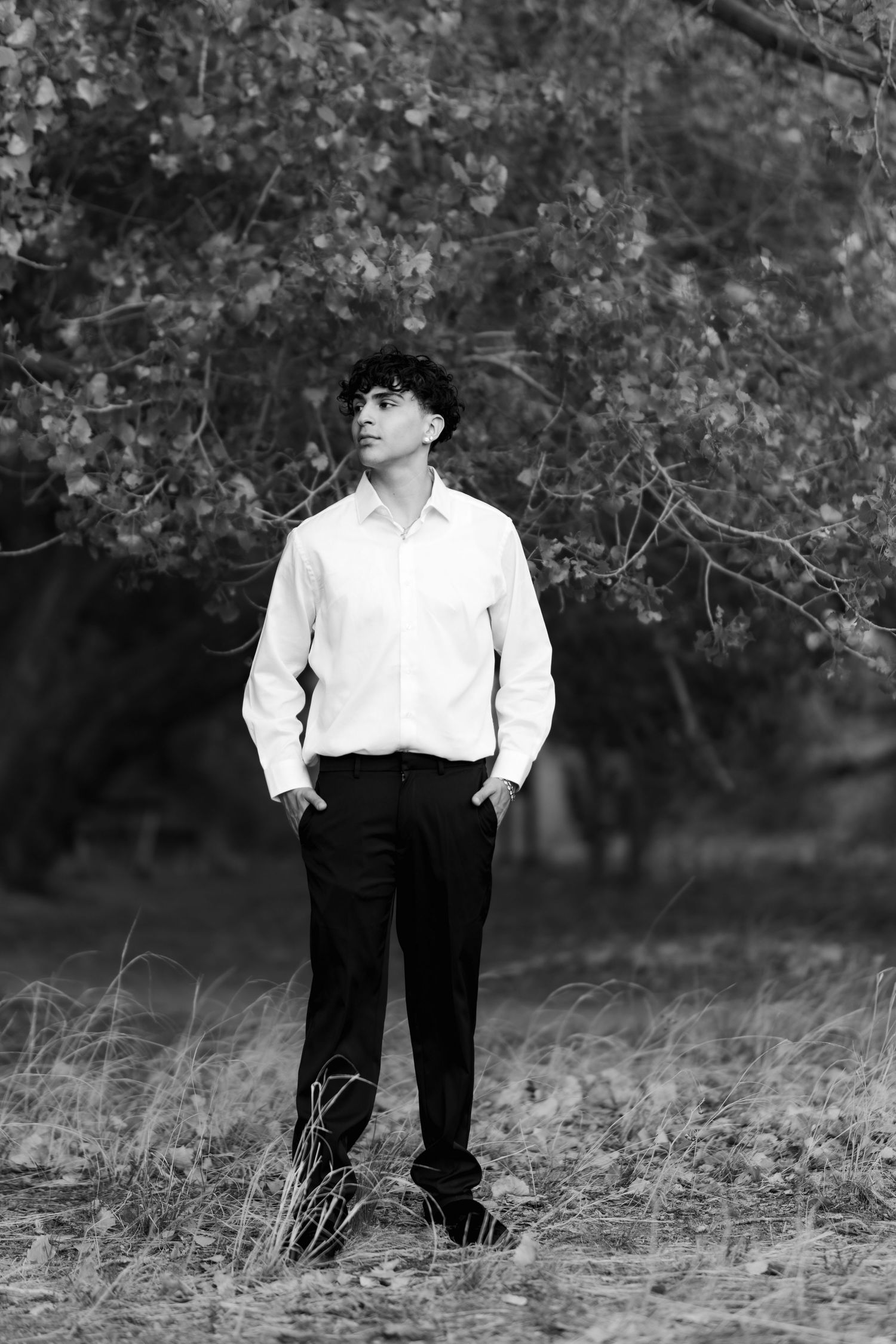 Black and white portrait of a person in a white dress shirt and dark pants standing in a natural outdoor setting during autumn.