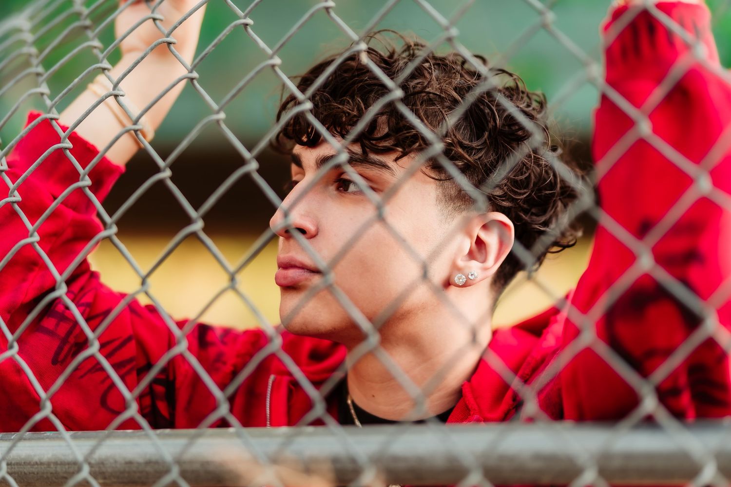 Baseball player in red uniform looks through dugout fence during game.