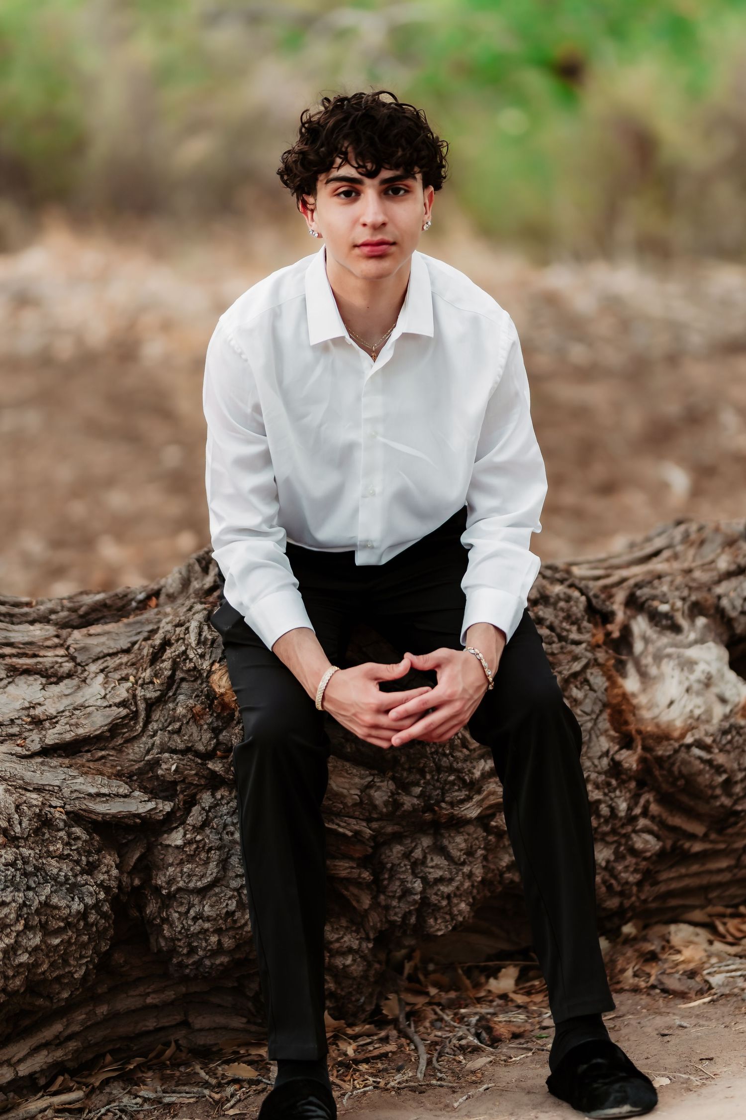 Person in white button-down shirt and dark pants sitting on fallen tree trunk in natural setting.