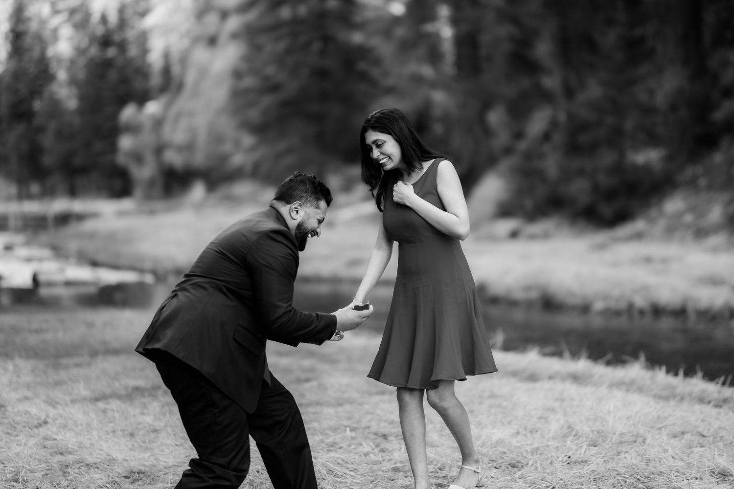 Romantic black and white photo captures playful proposal moment in outdoor meadow setting.
