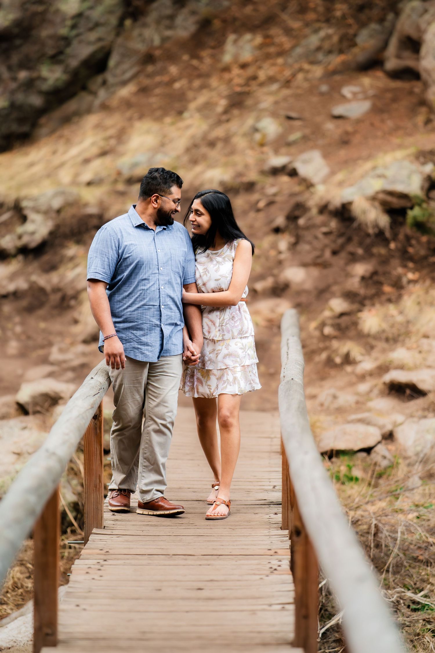 A couple sharing a tender moment while standing on a wooden bridge in a rocky landscape.