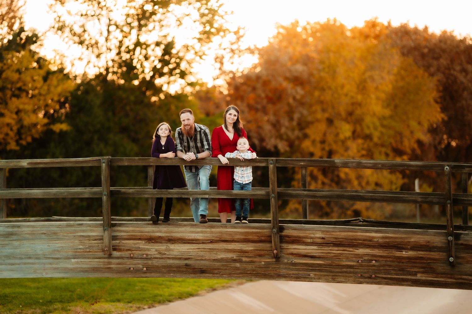 A couple sits on a wooden bridge surrounded by vibrant autumn foliage during golden hour sunset.