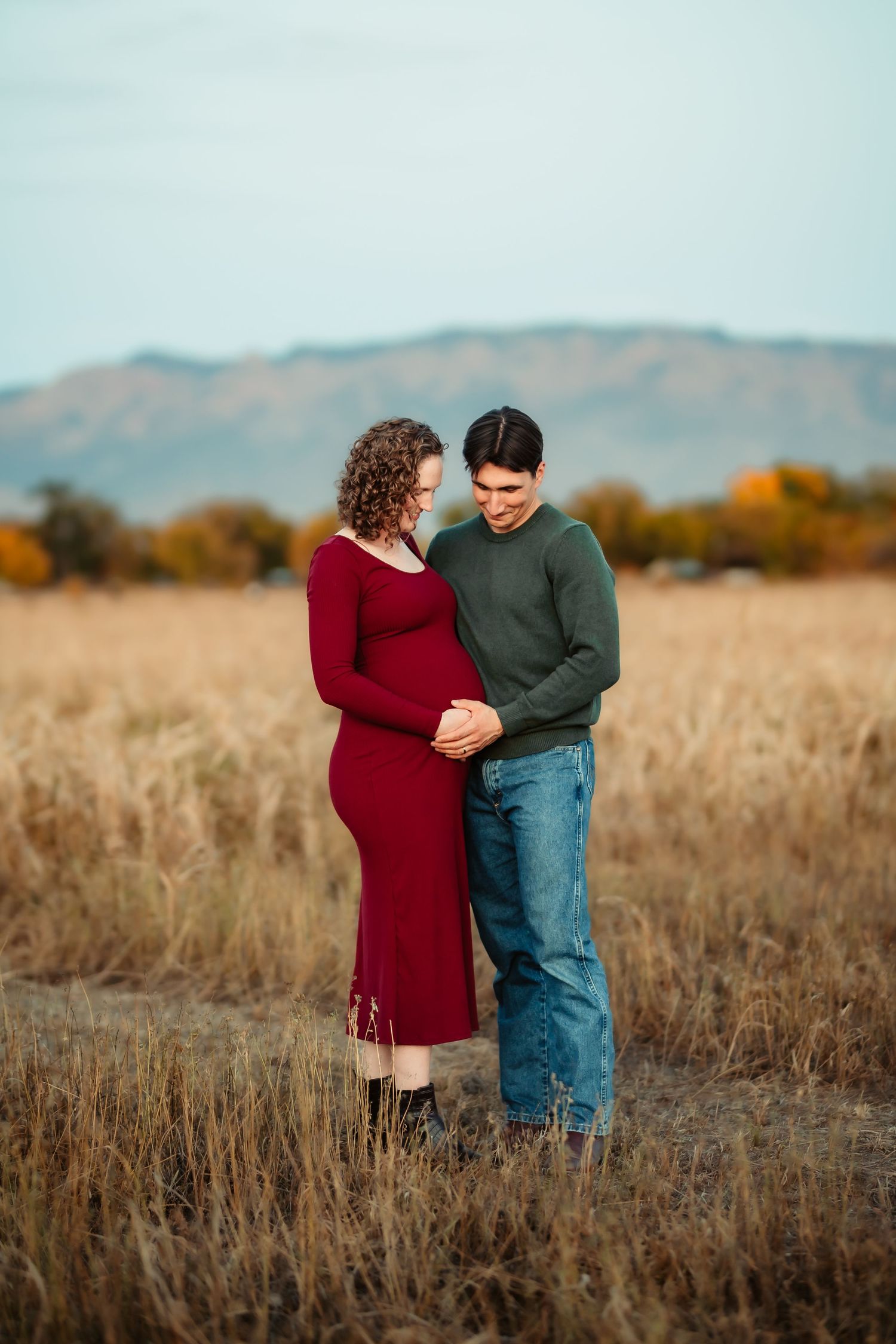 A couple dances together in a golden autumn field with mountains visible in the background at sunset.