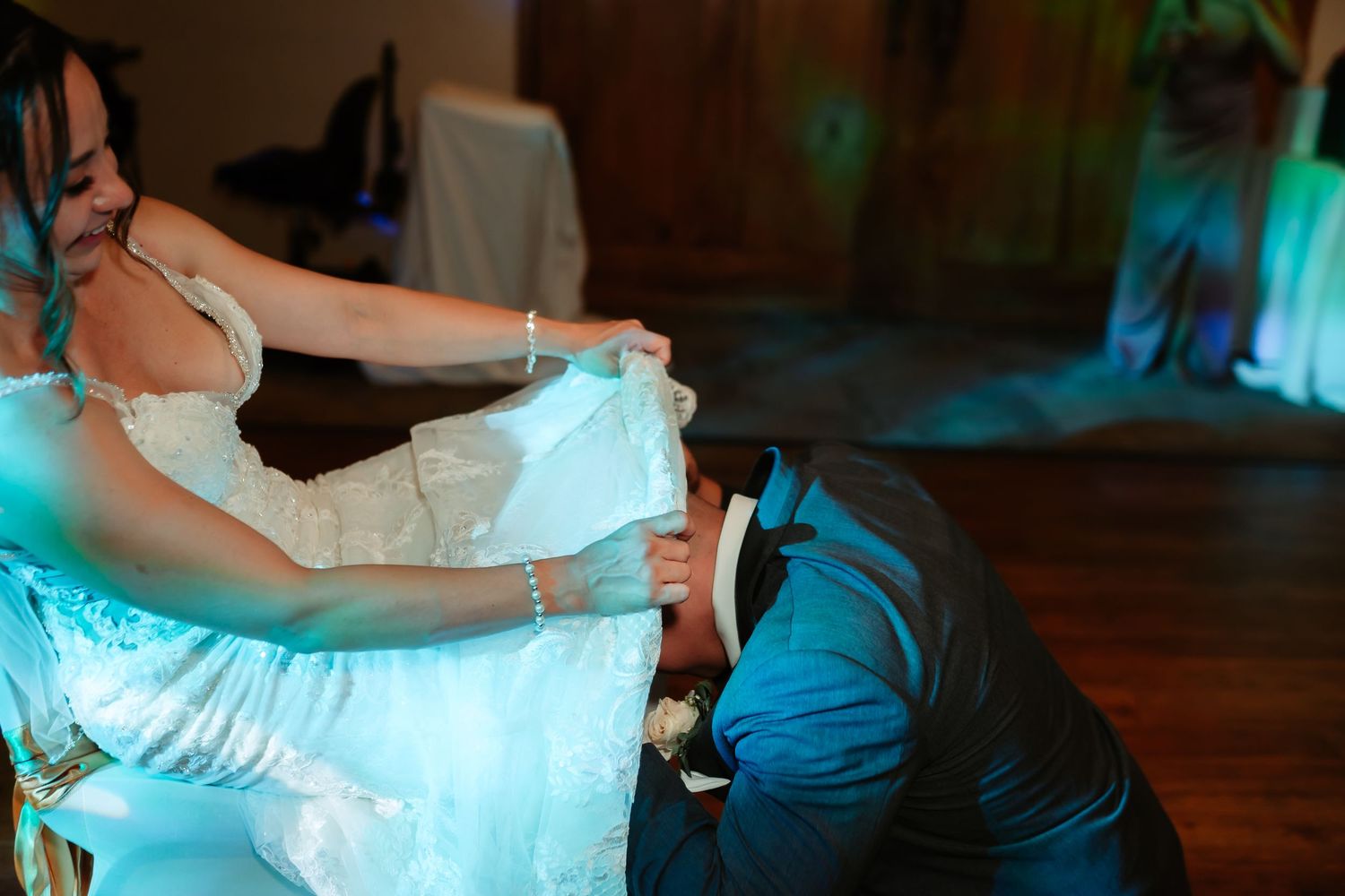 A bride in a white wedding dress twirls on the dance floor under atmospheric blue lighting at a reception.
